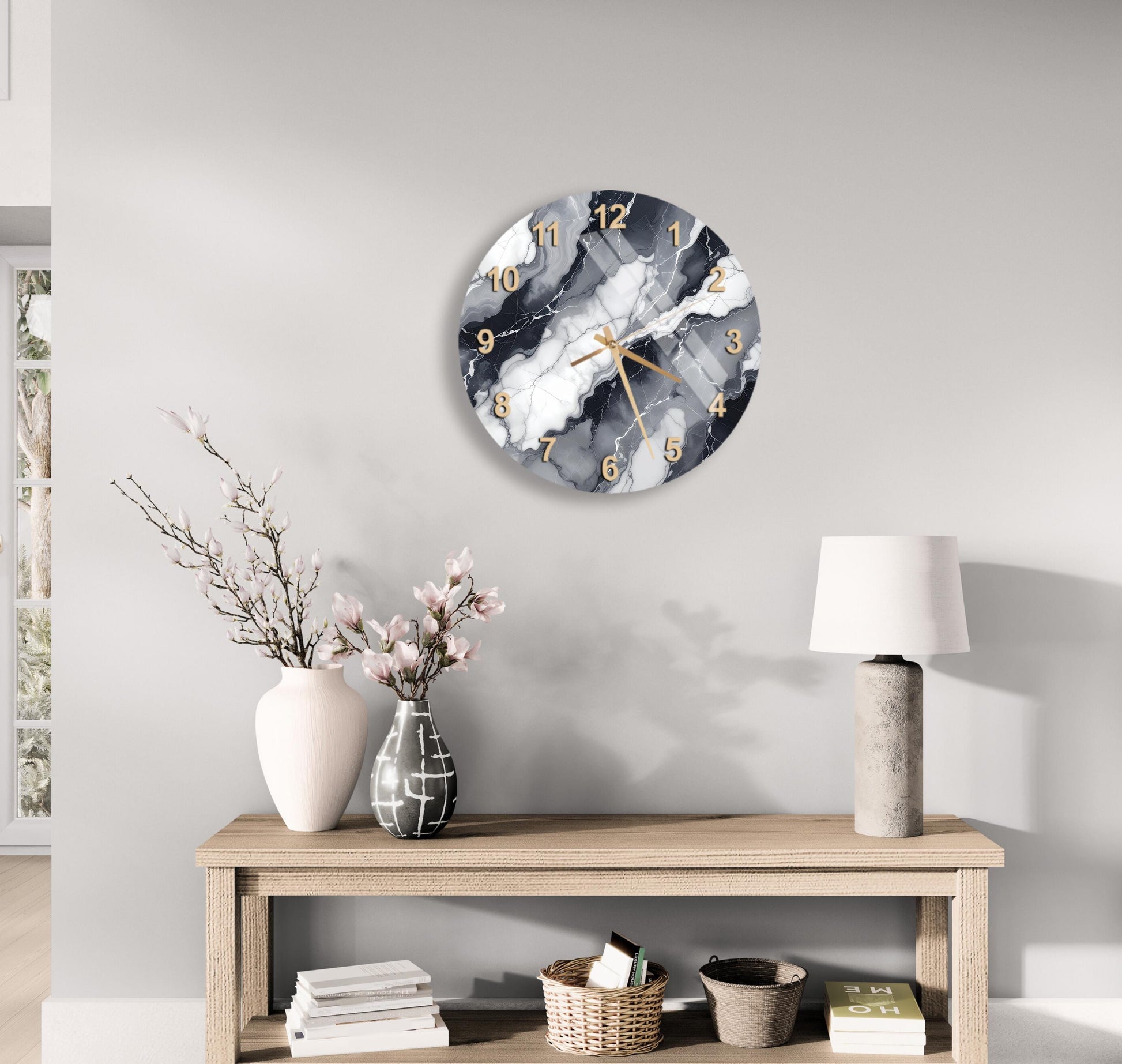 a modern living room with a wooden console table, a round wall clock with a marble-like design, a lamp, a vase with pink flowers, and a stack of books.