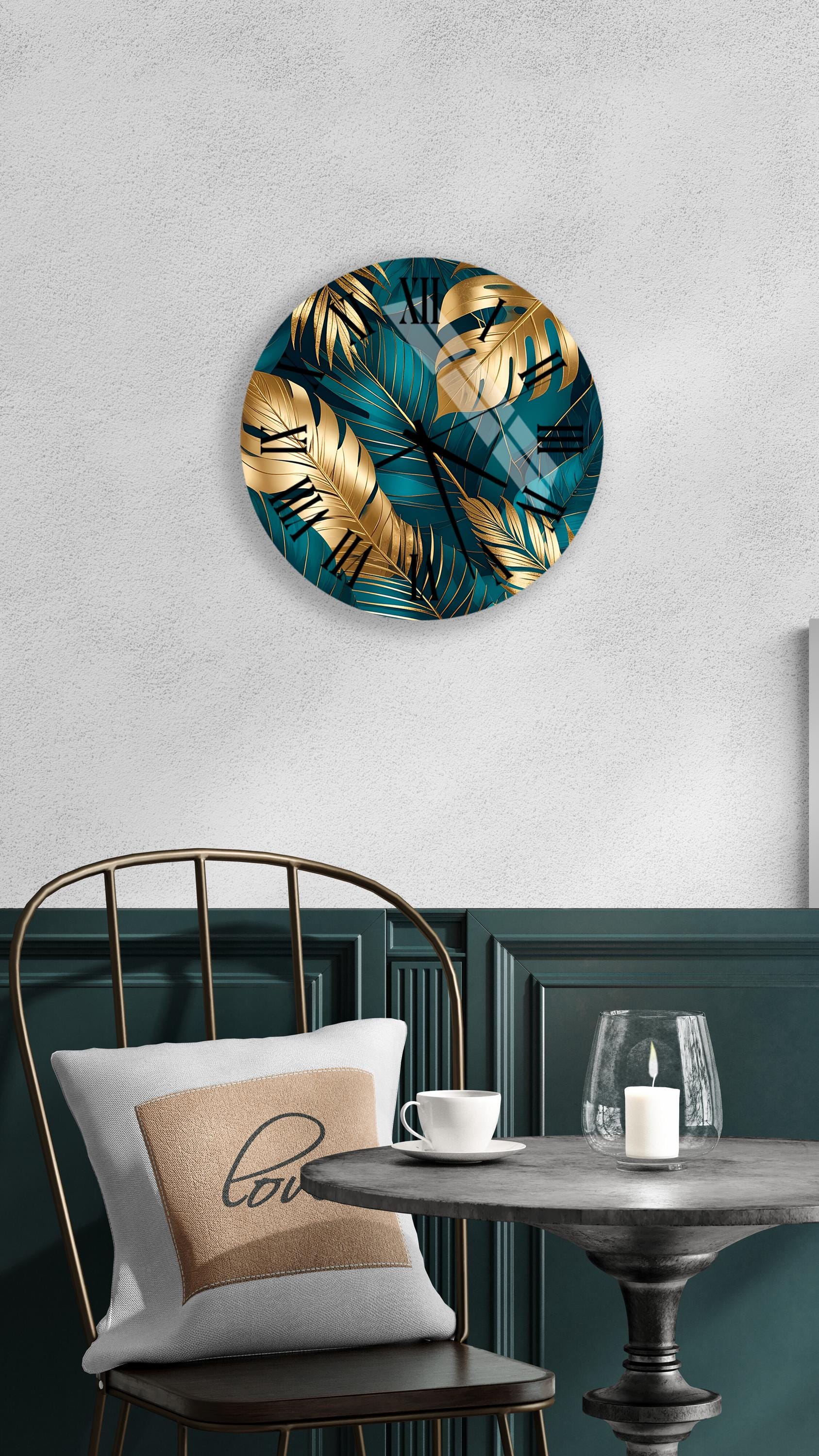 a modern and stylish interior design with a round wall clock featuring a tropical leaf pattern in shades of blue and gold, a white pillow with a black "love" message, a black metal chair, and a small table with a candle and a glass.