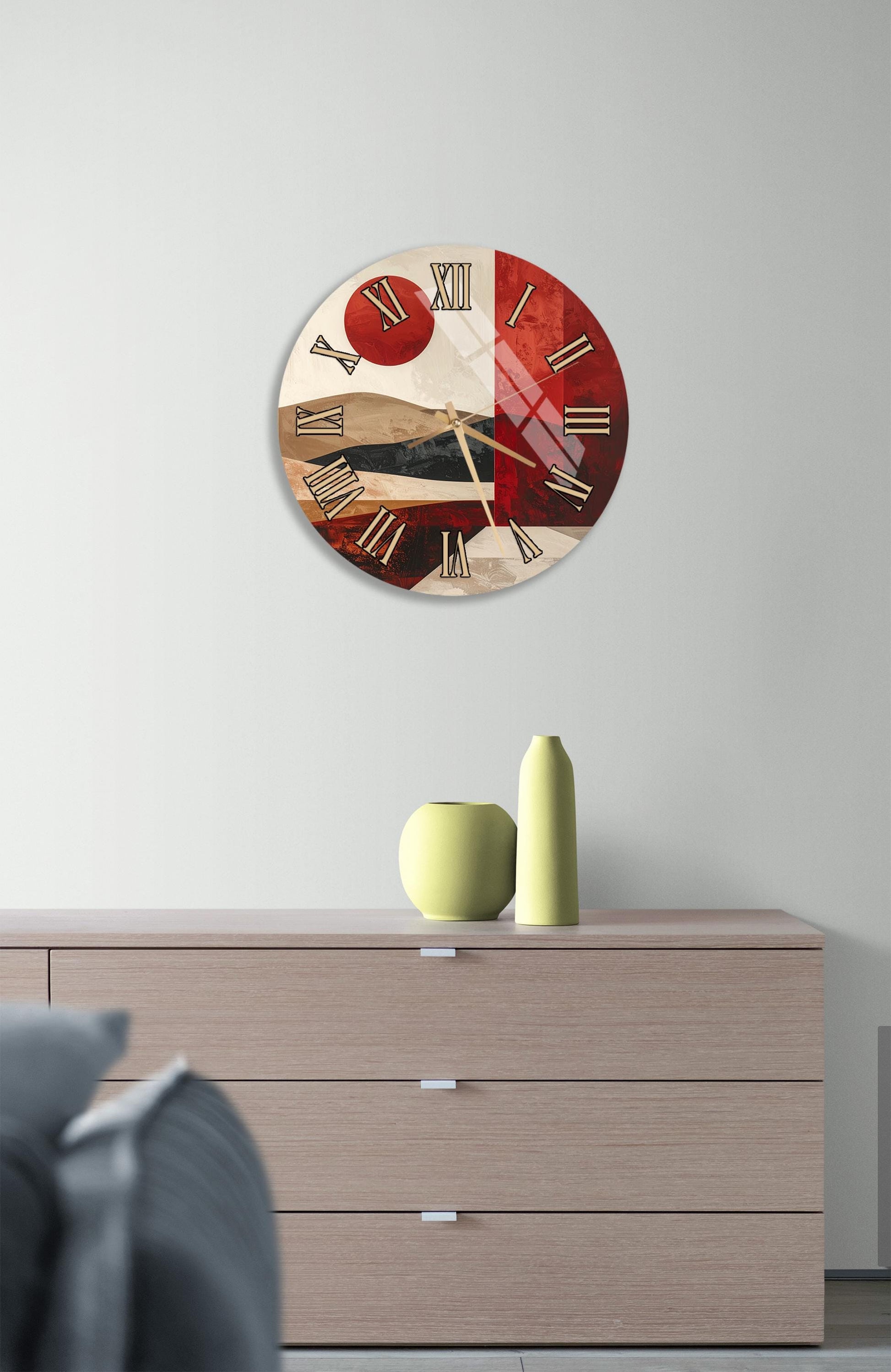 a modern wall clock with a red and white color scheme, mounted on a wall above a wooden dresser. The dresser has three drawers and a vase on top.