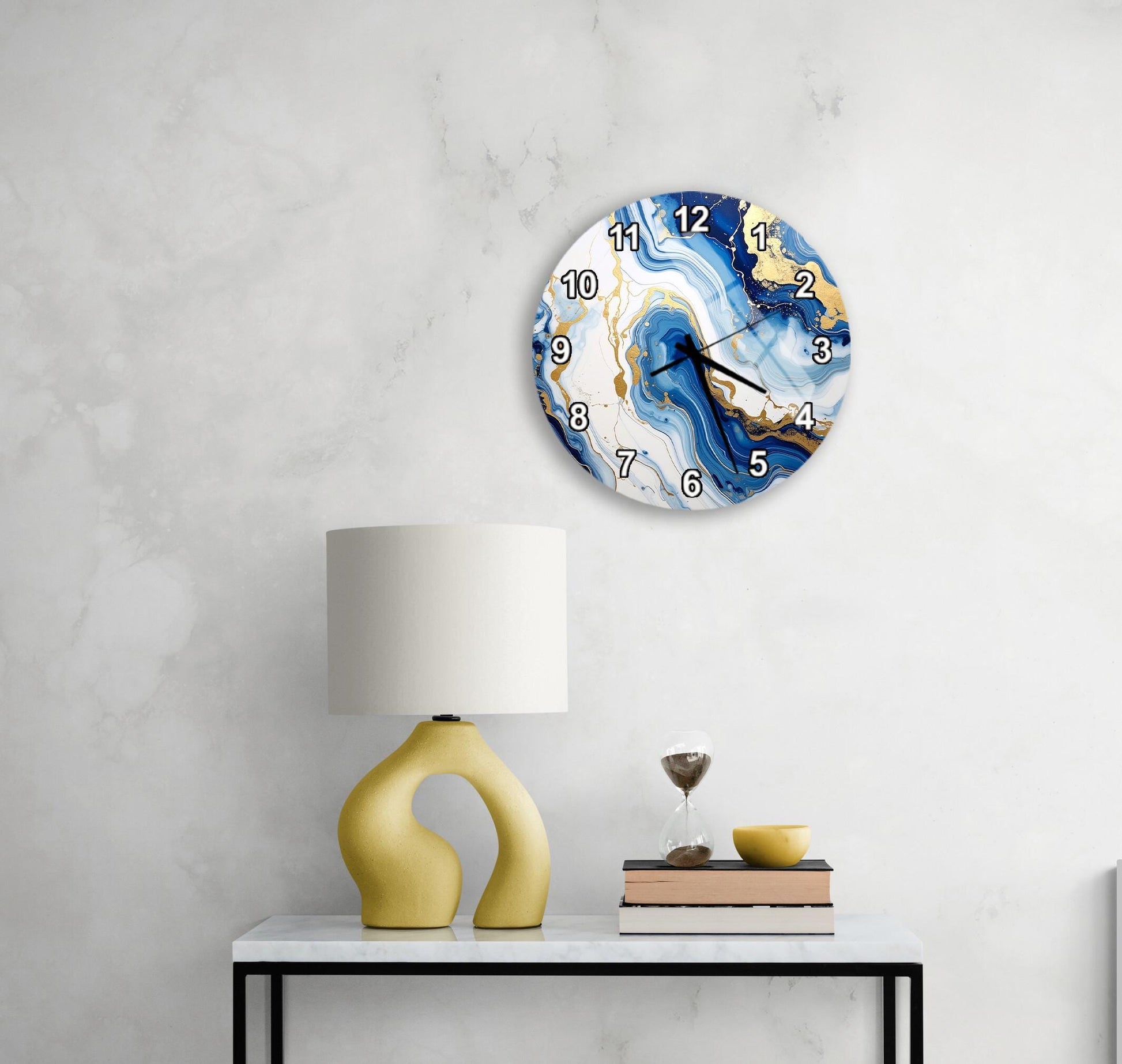 a white marble wall with a round clock featuring a blue and white marble design, a yellow lamp with a unique curved base, and a stack of books on a white table.