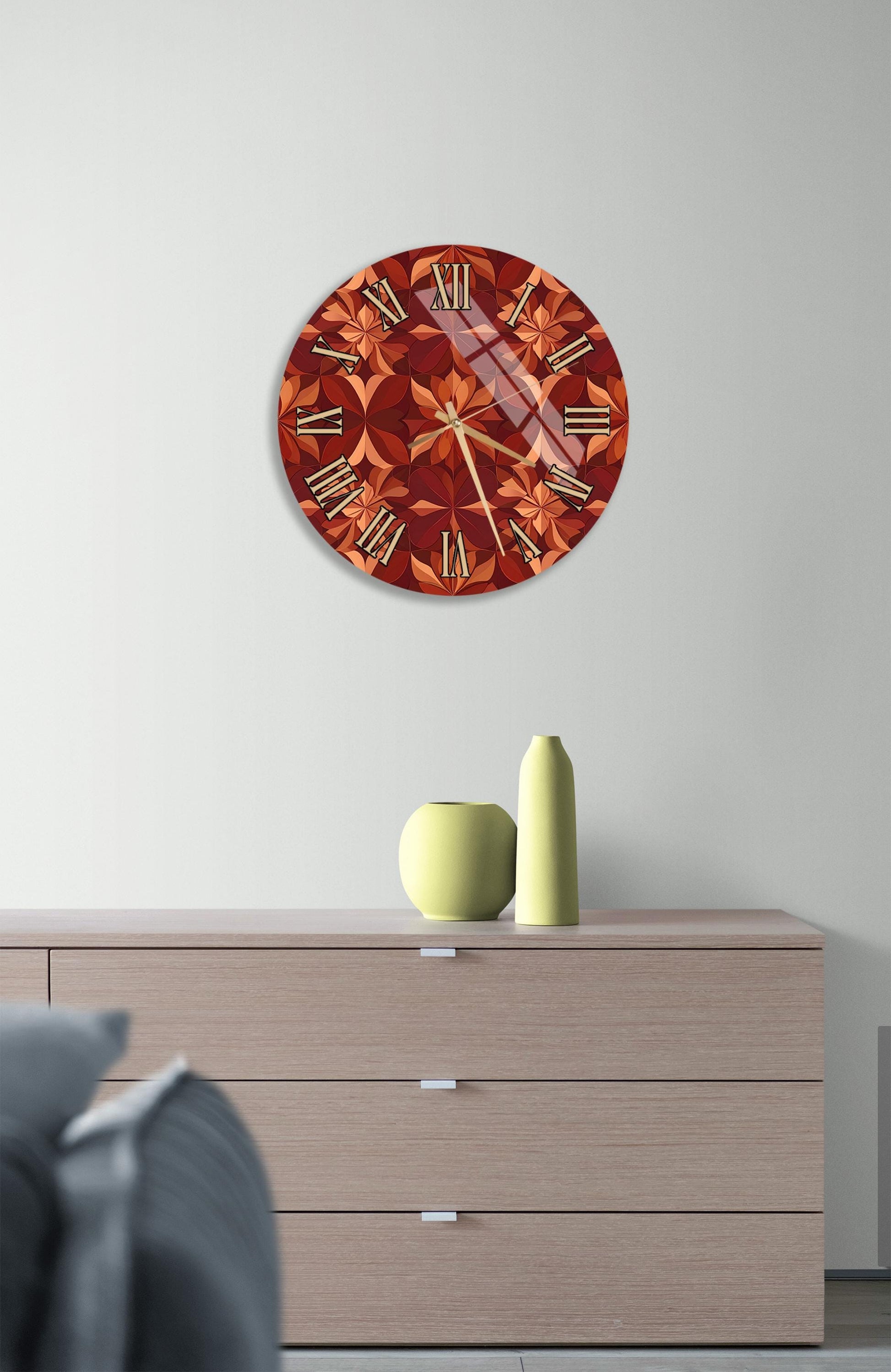 a wall clock with a floral design, mounted on a wall above a wooden dresser with a vase and a small green pot on top.