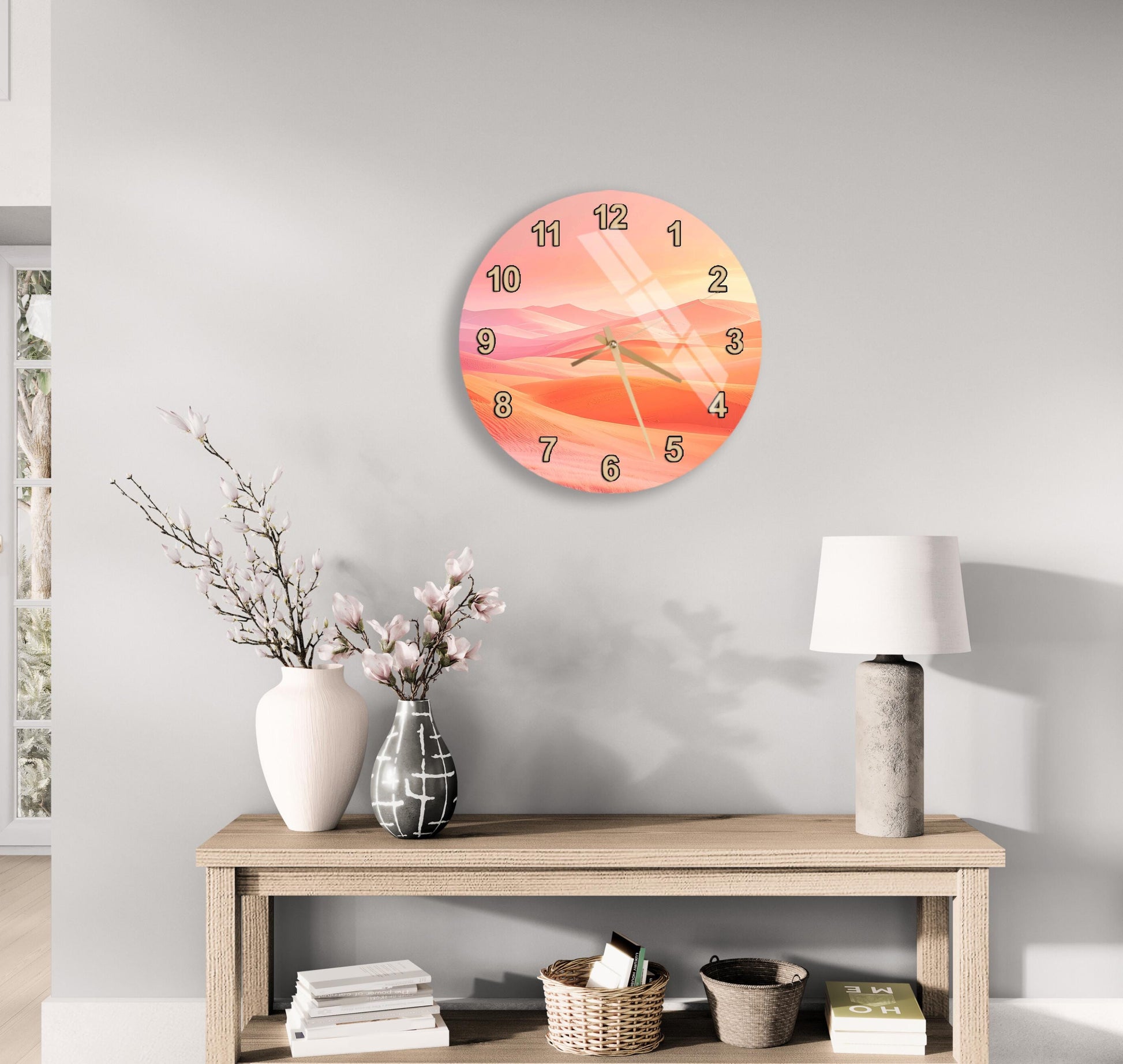 a wall clock with a sunset design, a wooden table with a lamp, a vase with flowers, and some books on a shelf.