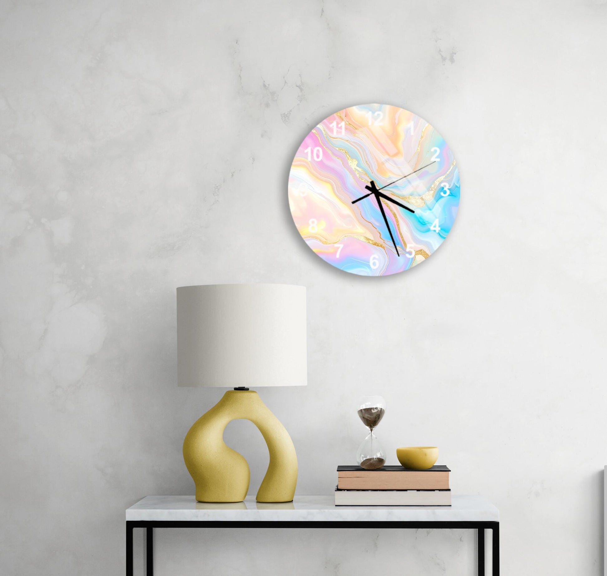 a white wall with a round clock featuring a colorful abstract design hanging above a white table with a yellow lamp and a stack of books.