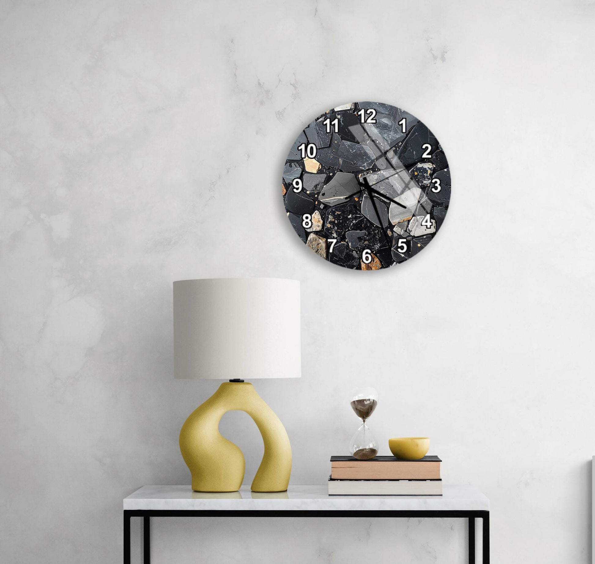 a modern black and white clock with a unique design, mounted on a white wall above a white table with a yellow lamp and a stack of books.