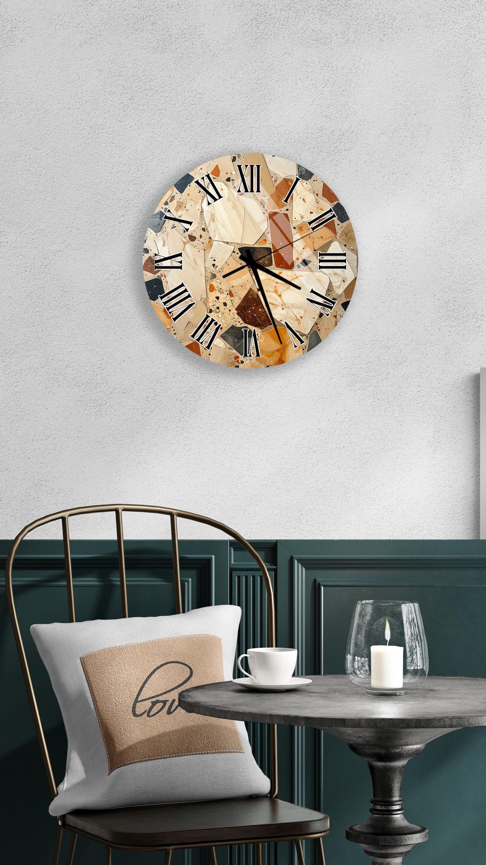a round wall clock with a marble-like design, mounted on a wall above a table with a white tablecloth. The table has a glass candle and a white coffee cup on it. A white pillow with the word "love" printed on it is also present on the table.