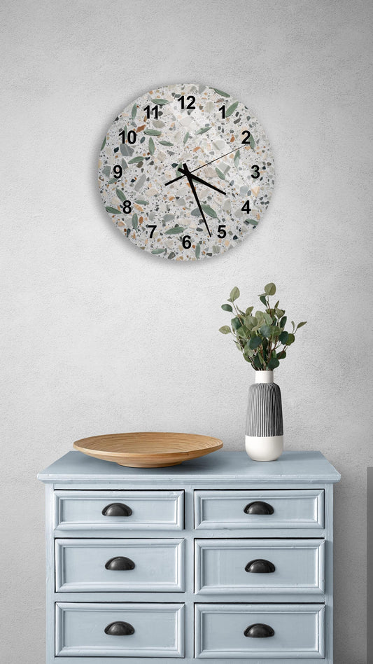 a wall clock with a unique, speckled design, mounted on a wall above a light blue wooden dresser with six drawers. The dresser also has a vase with greenery on it, and a wooden plate on top.