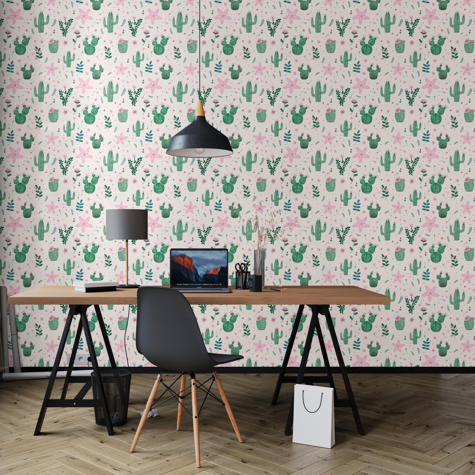 a workspace with a laptop, a wooden desk, and a black chair. The workspace is set against a wall with a repeating pattern of cacti and other plants, creating a vibrant and lively atmosphere.