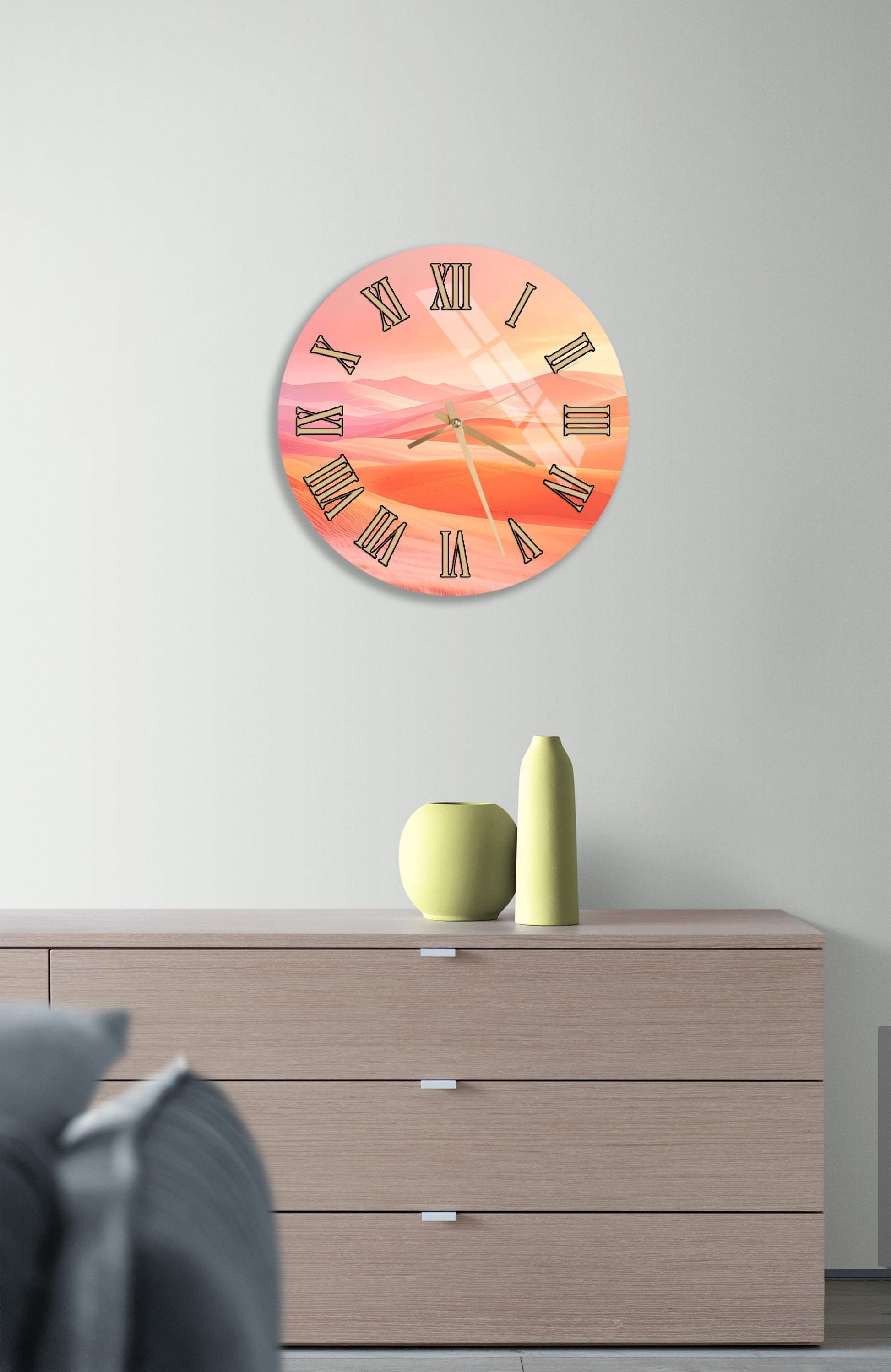 a wall clock with a sunset-themed design, mounted on a wall above a wooden dresser with a vase and a small sculpture on top.
