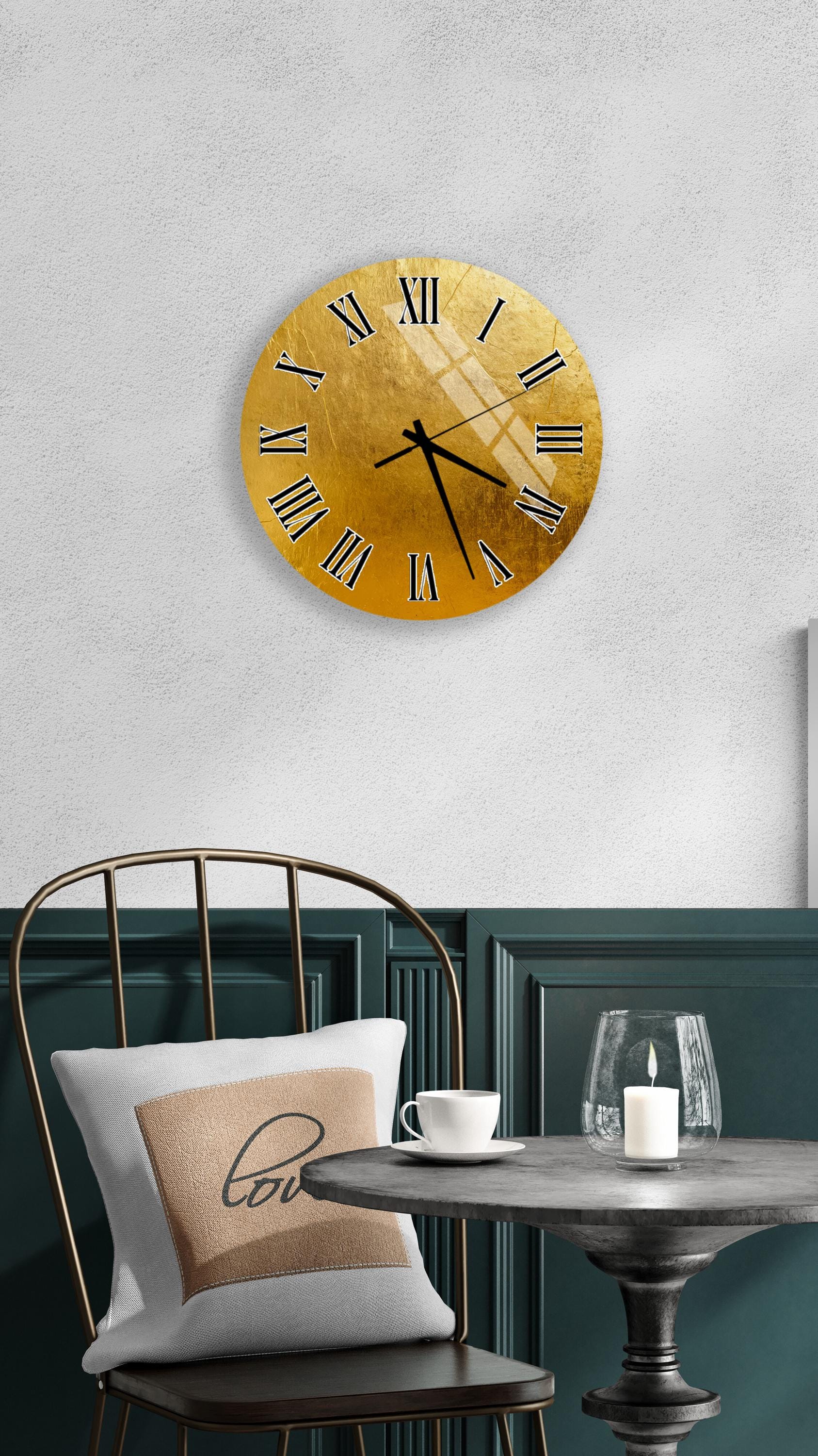 a modern interior design with a gold-colored clock mounted on a white wall above a black chair with a white pillow. The chair is positioned in front of a small round table with a glass of wine and a candle on it.