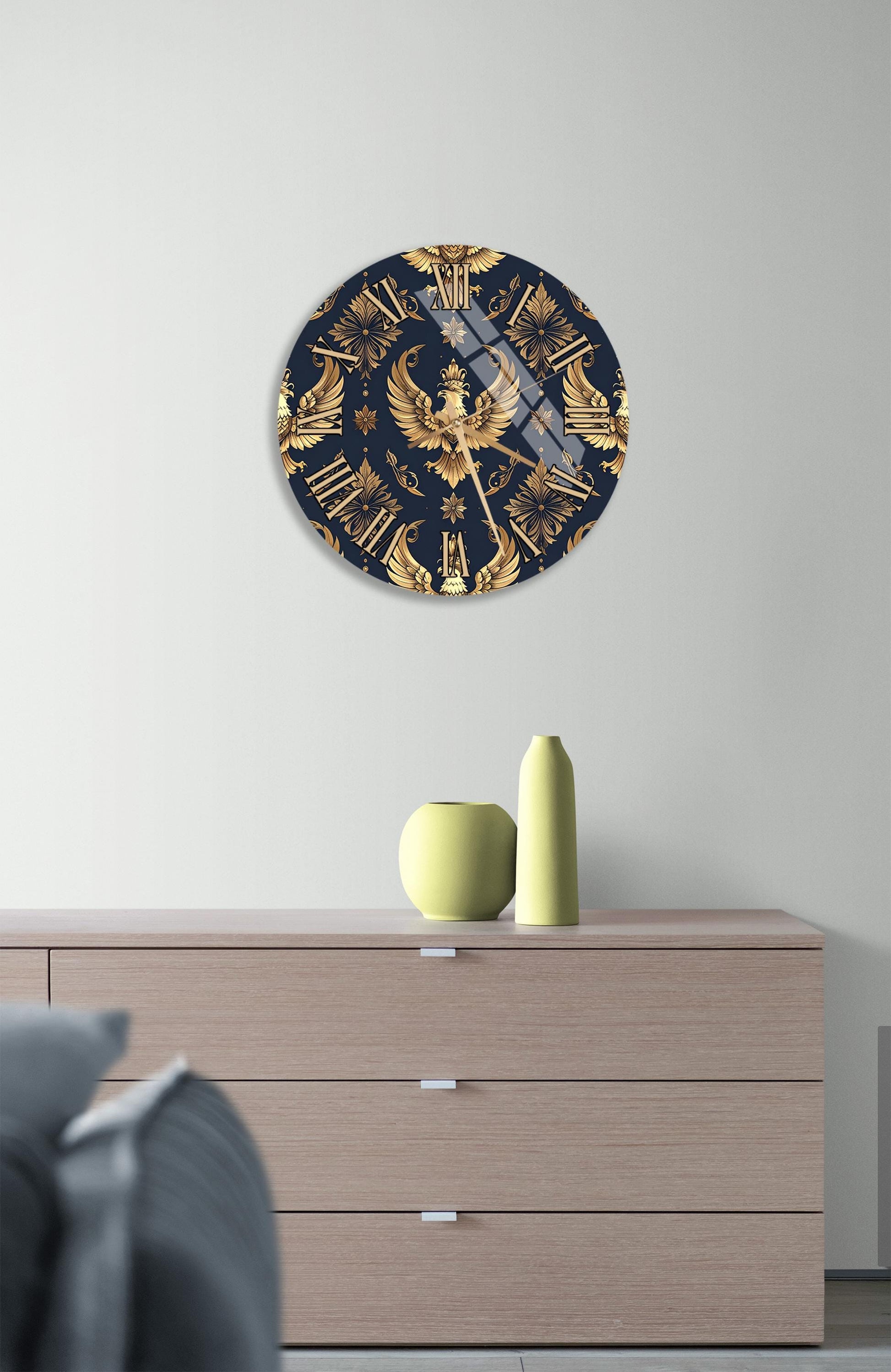 a wall clock with a gold and navy blue design, mounted on a wall above a wooden dresser with a vase and a small sculpture on top.