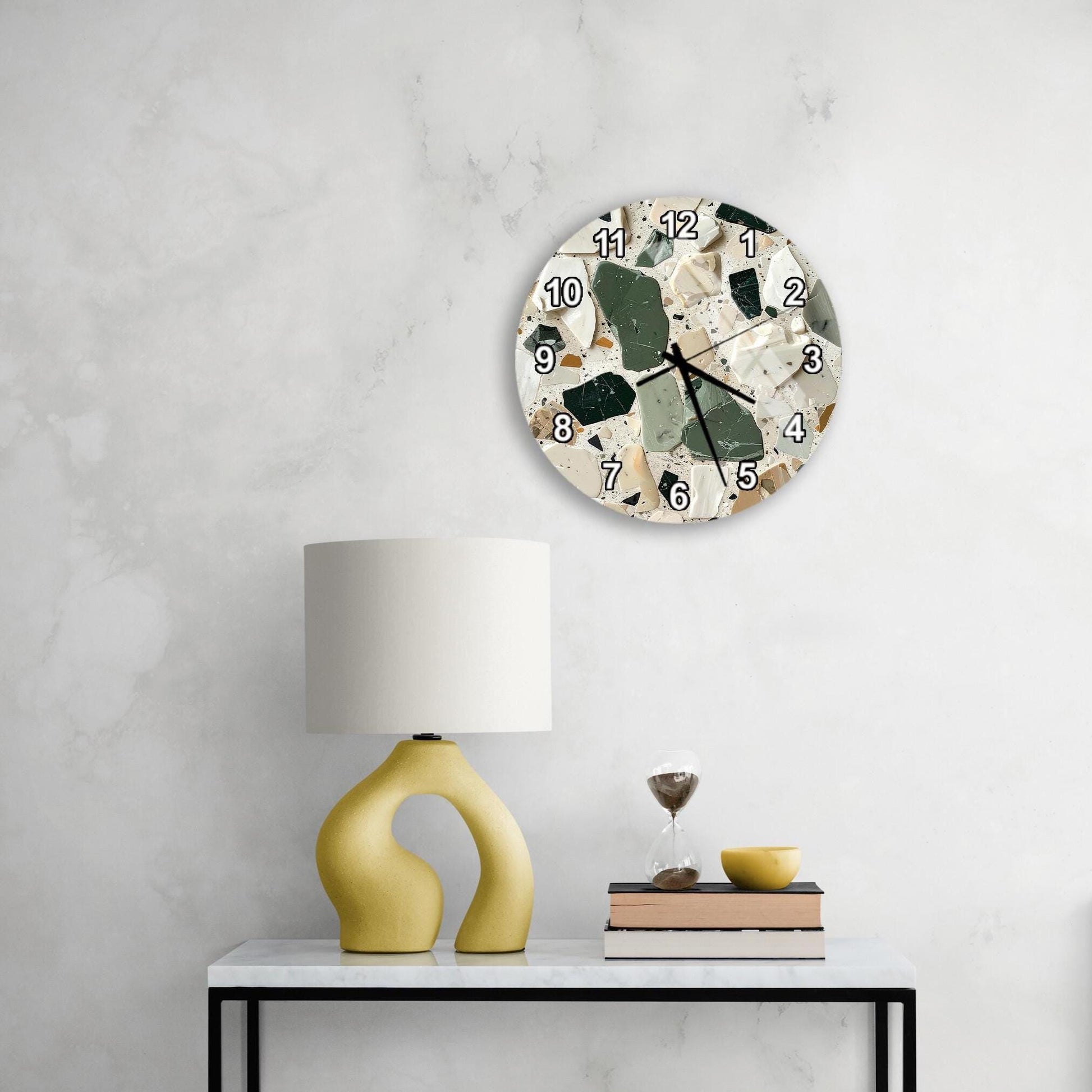 a modern, minimalist living space with a white marble wall, a round wall clock with a unique design, a yellow lamp with a curved base, and a small table with a book and a glass of wine.
