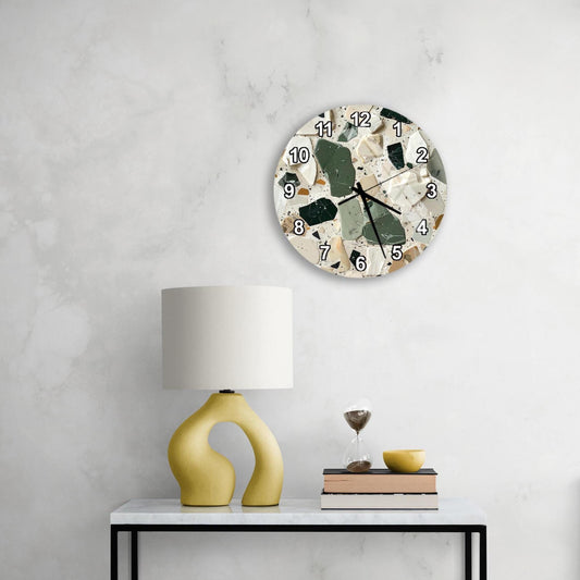 a modern, minimalist living space with a white marble wall, a round wall clock with a unique design, a yellow lamp with a curved base, and a small table with a book and a glass of wine.