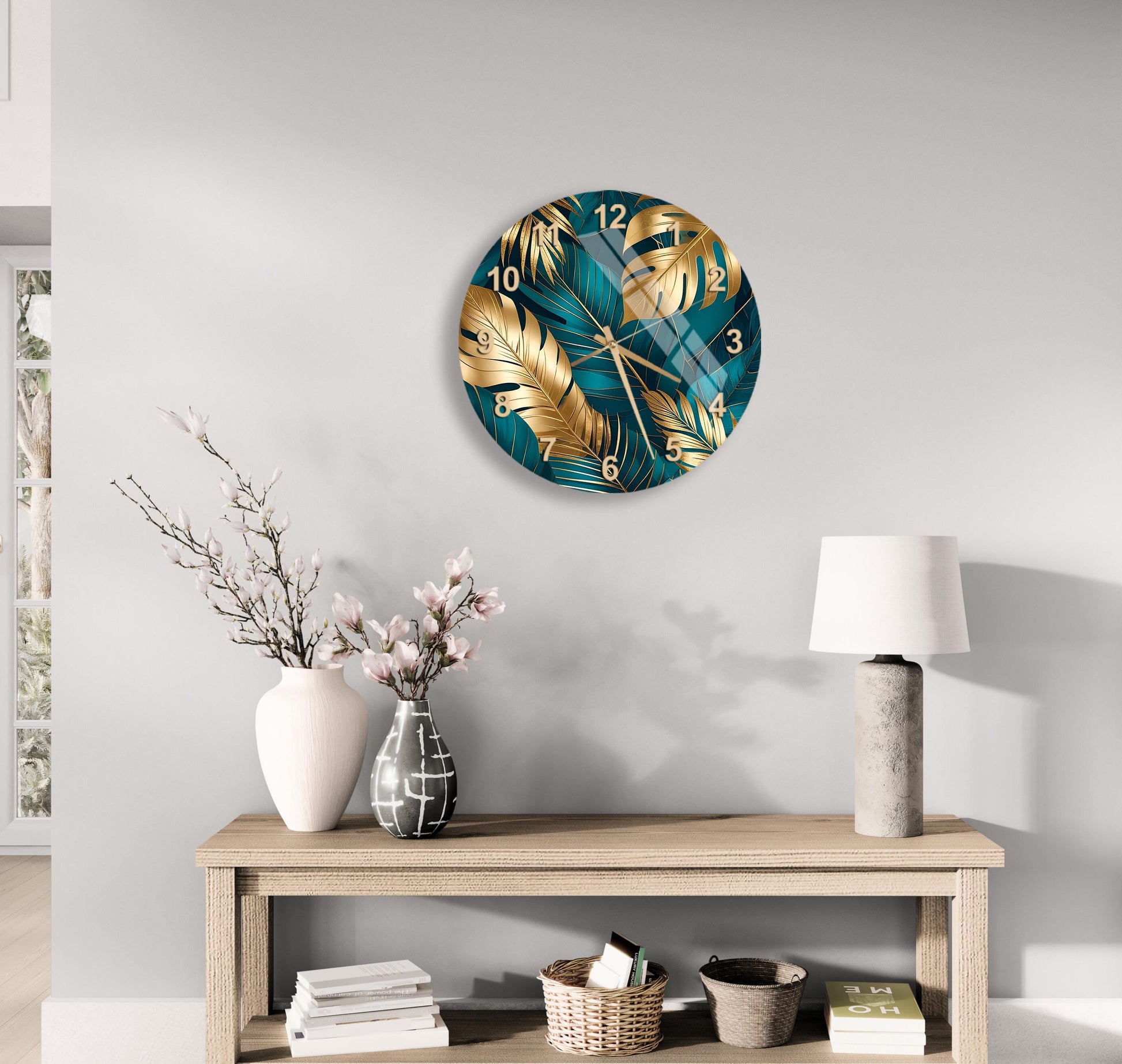 a modern living room with a large round clock with a tropical leaf design on the wall above a wooden table. The table has a vase of flowers, a lamp, and some books on it.