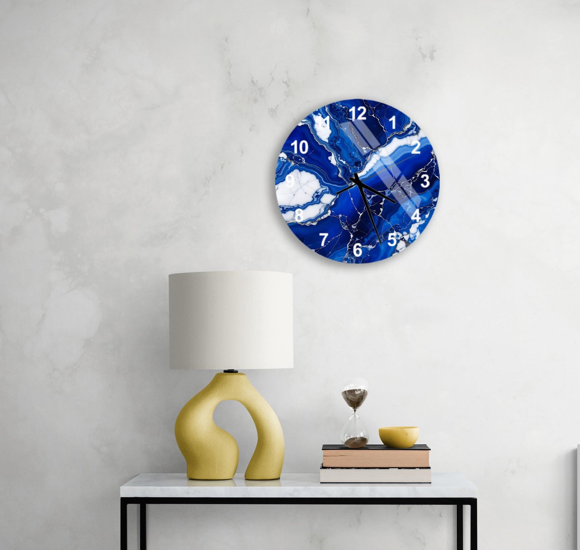 a modern living room with a white marble wall, a round clock with a blue and white marble design, a yellow lamp with a unique curved base, and a small table with a book and a glass of water.