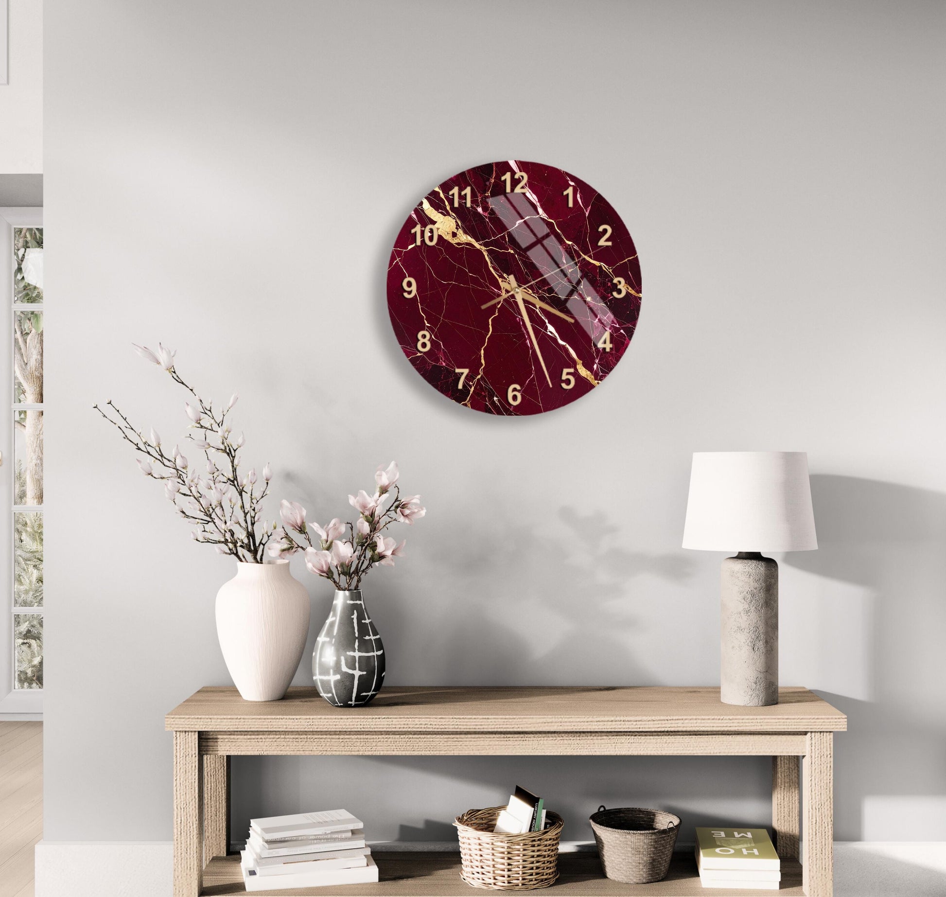 a modern living room with a wooden table displaying a white vase with pink flowers, a white lamp, and a round clock with a maroon and gold design.