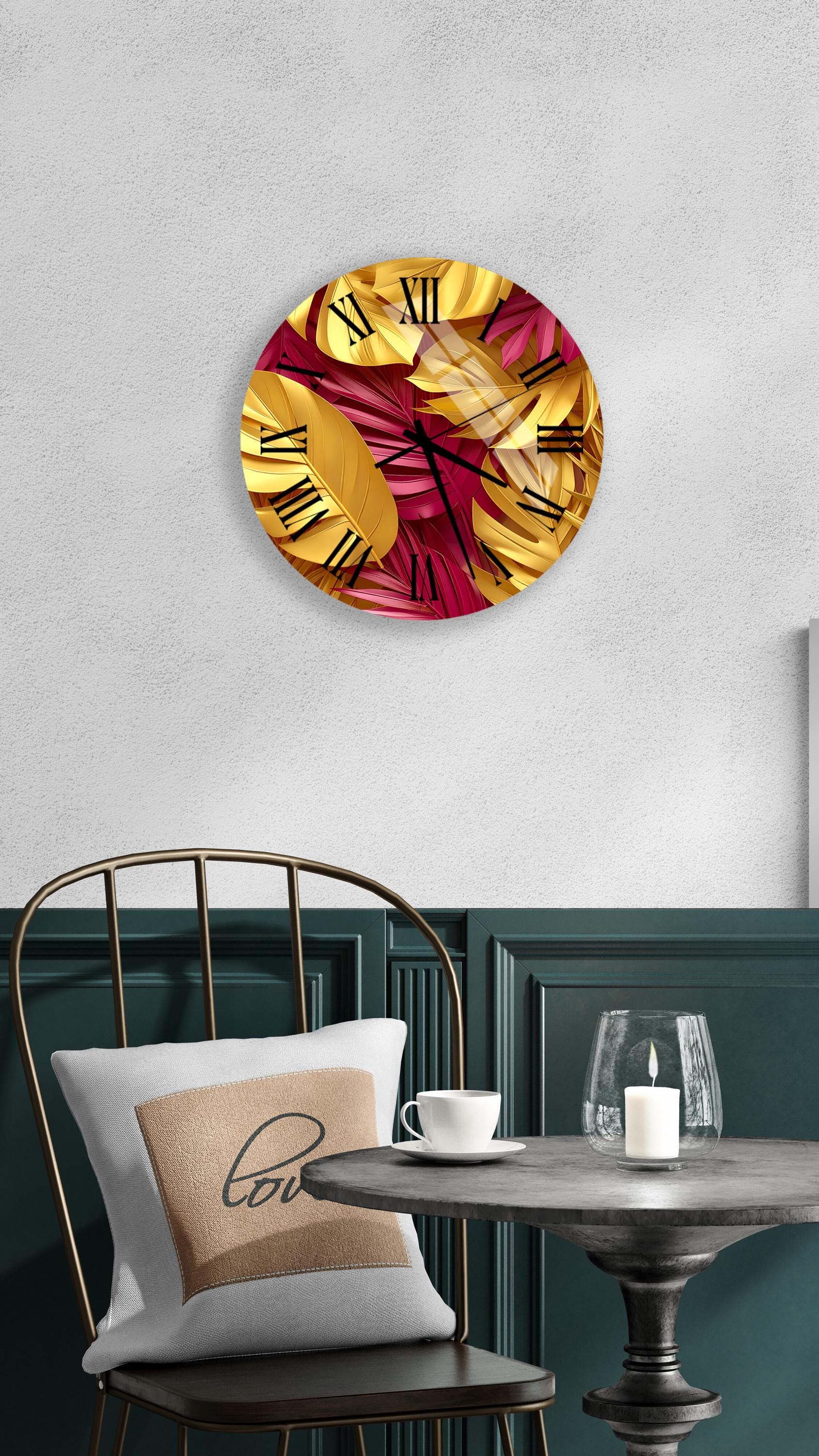 a round wall clock with a gold and red leaf design, mounted on a white wall above a dining table with a white tablecloth.