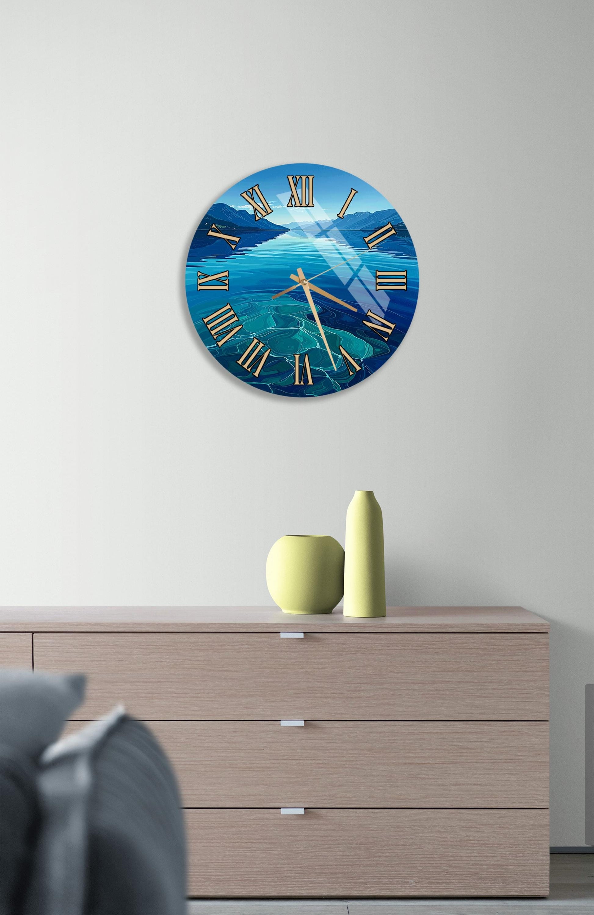 a wall clock with a blue ocean scene on its face, mounted on a wall above a wooden dresser with a vase and a small sculpture on top.