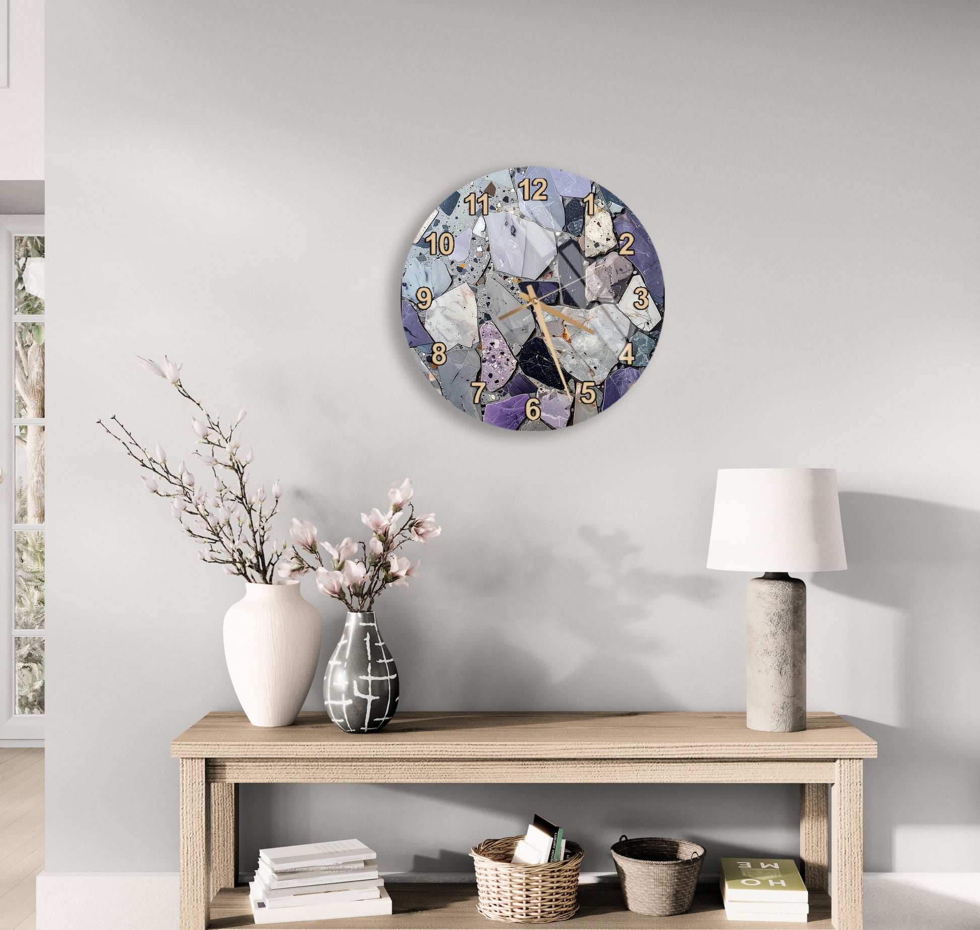 a wall clock with a unique design, a wooden table with a lamp, a vase with flowers, and some books on a shelf.