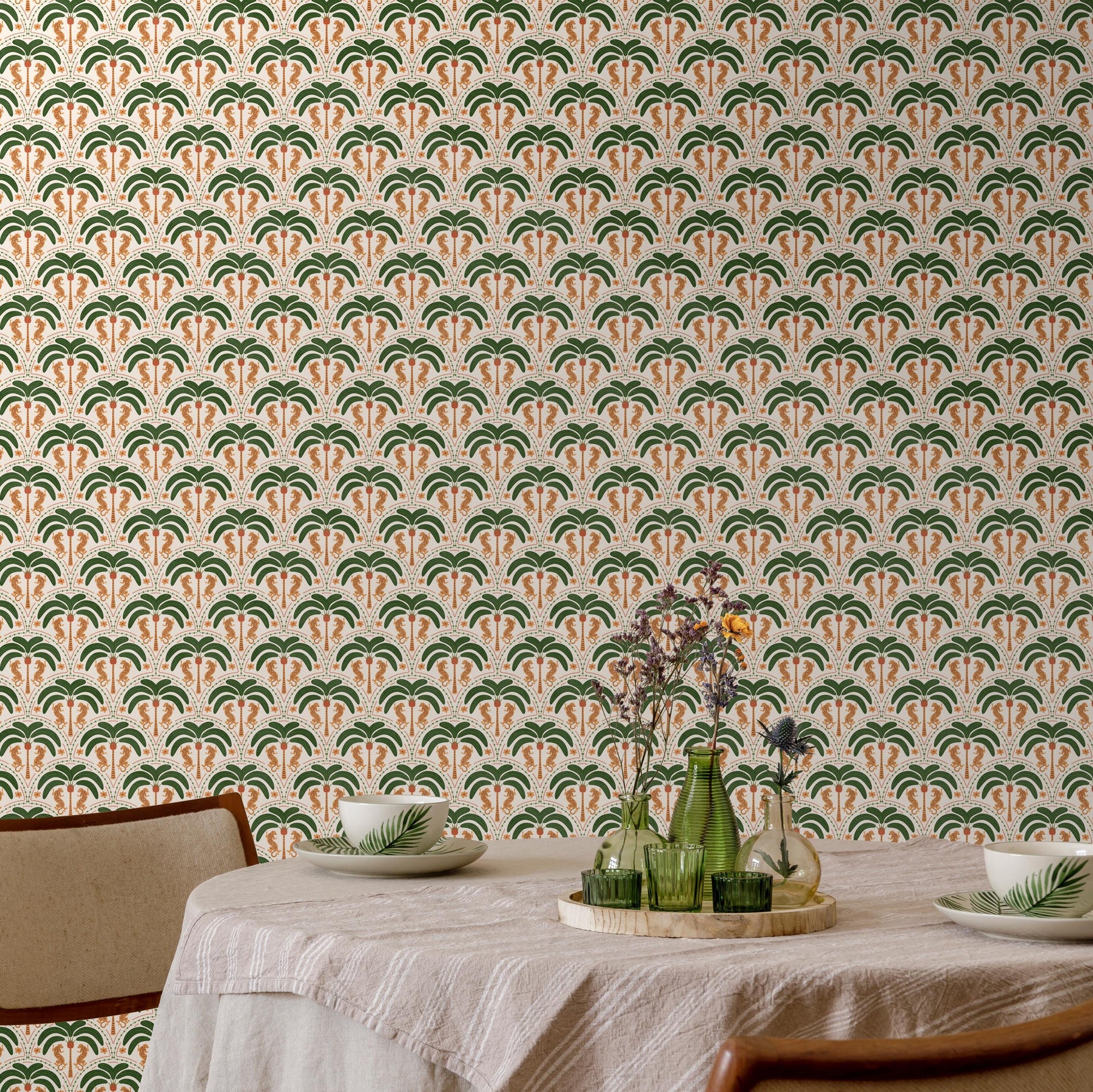 a dining table set with a white tablecloth, two white plates, and two green vases with flowers. The table is positioned against a wall with a repeating pattern of palm trees and leaves in shades of green and orange.