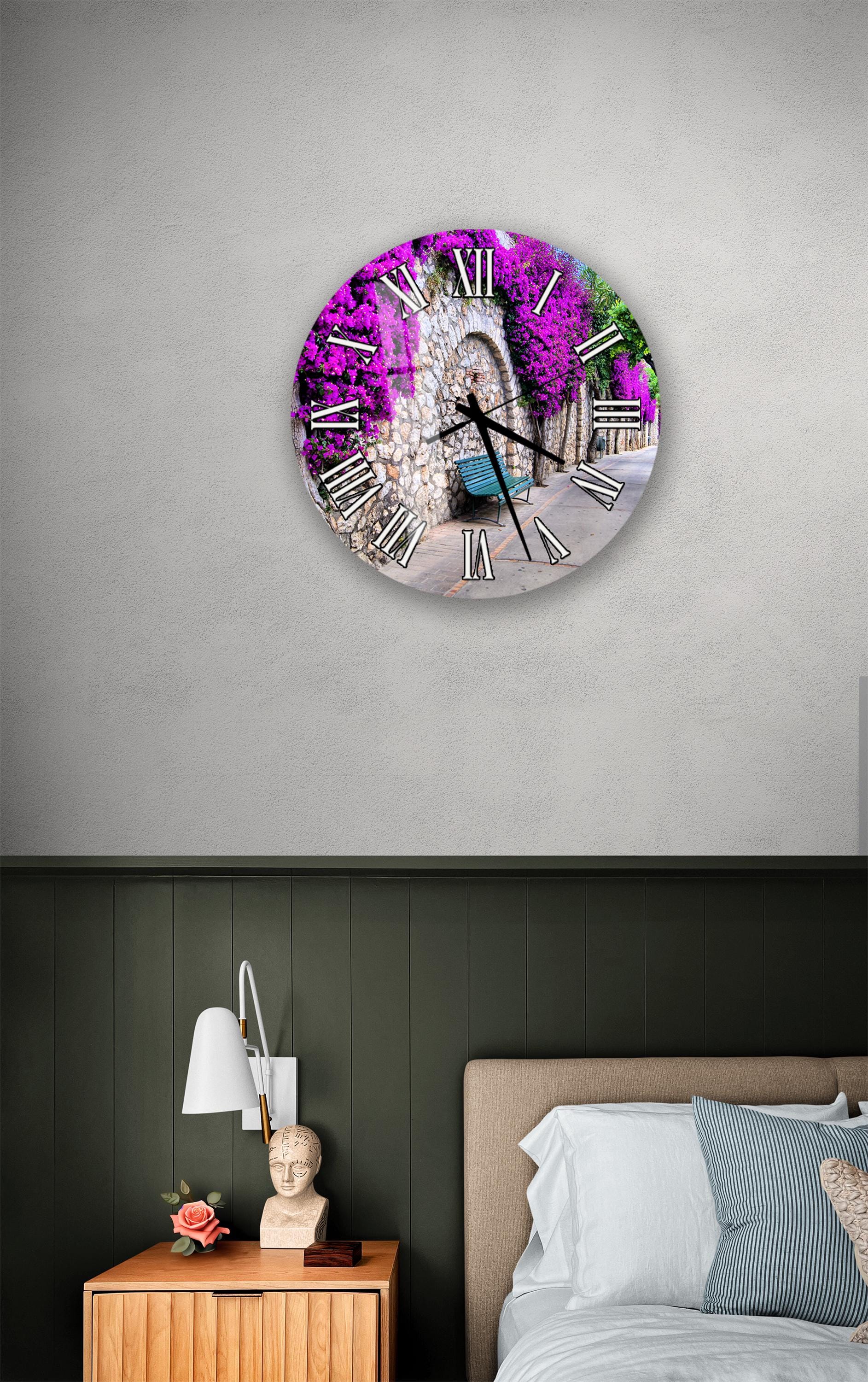 a clock with a purple floral design on a wall above a bed with a white headboard.