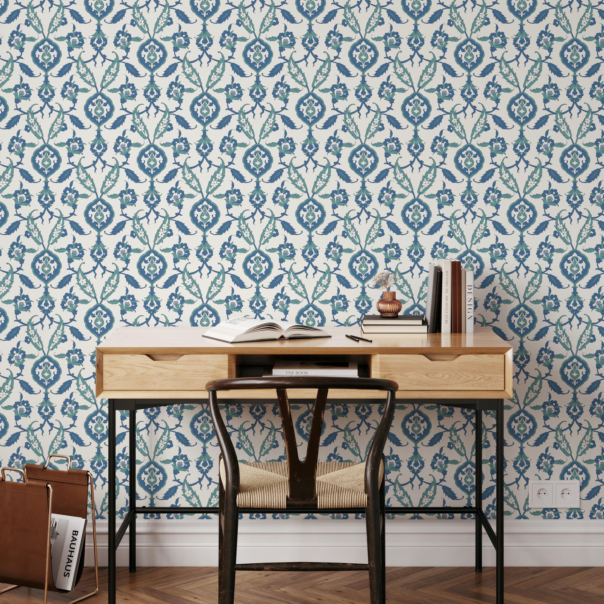 a wooden desk with a black chair, a wooden shelf with books, and a patterned wallpaper in the background.