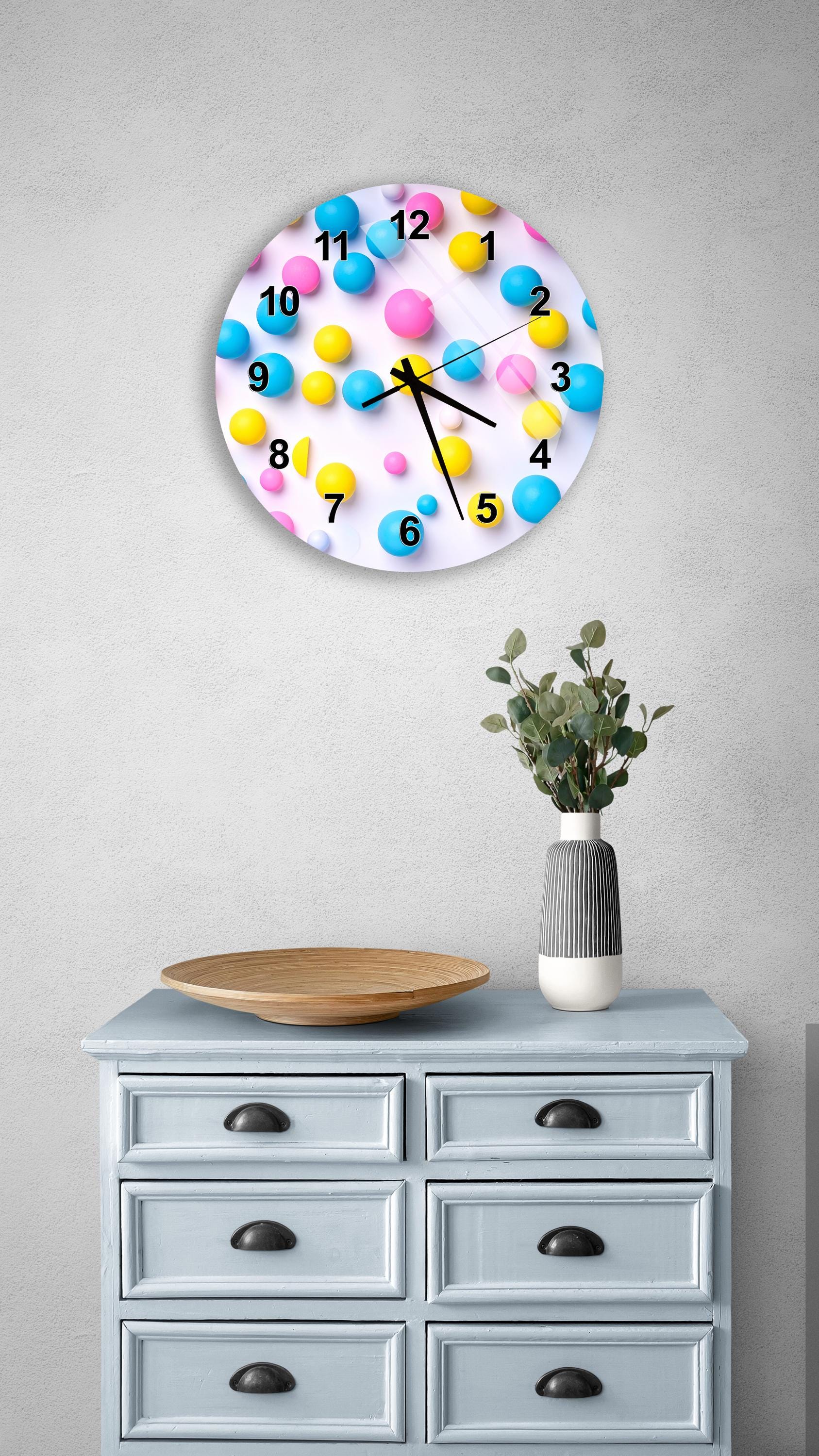 a wall clock with a colorful design of bubbles and numbers, mounted on a wall above a wooden dresser with drawers.