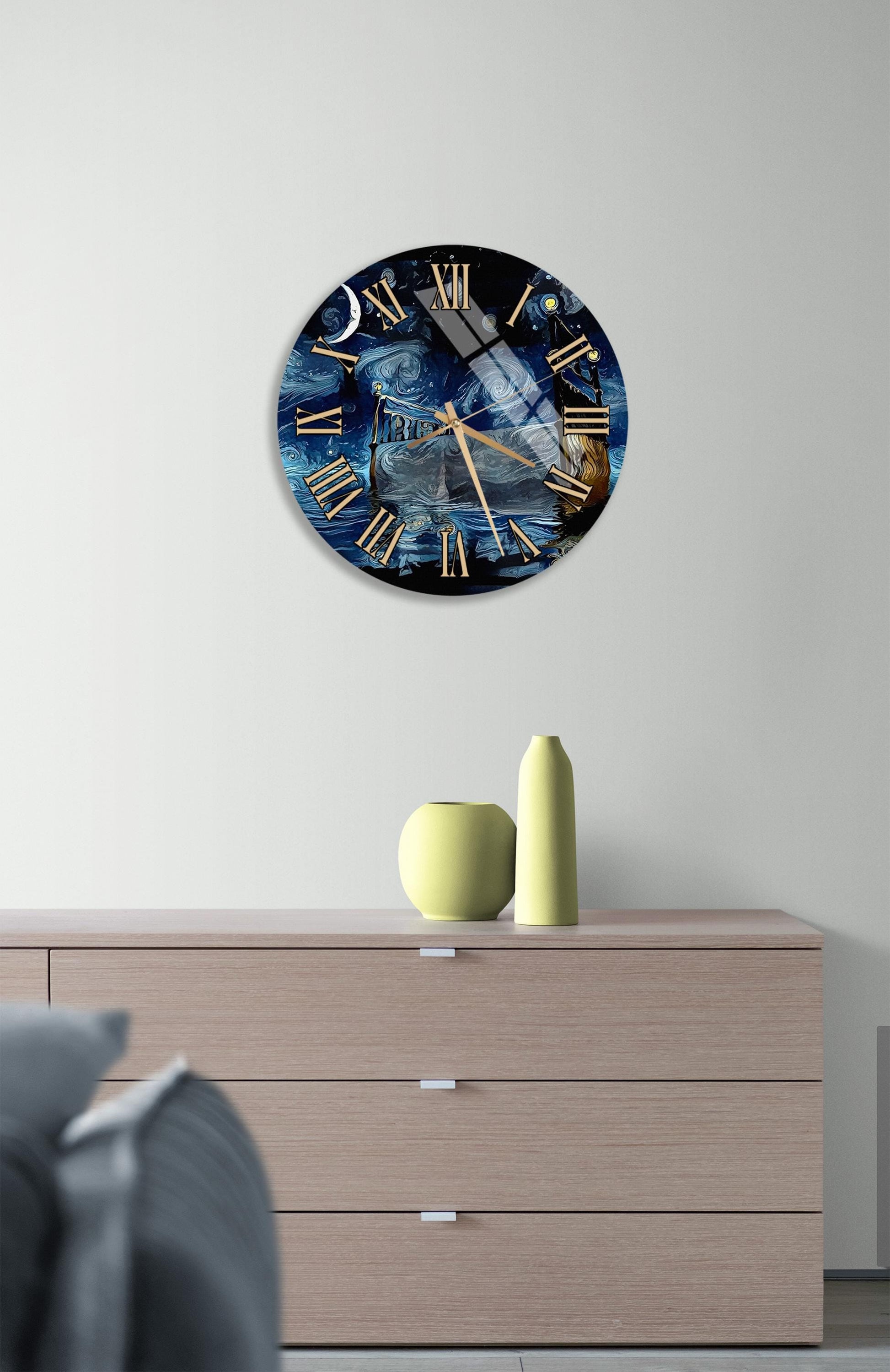 a wall clock with a blue and black design, hanging on a wall above a wooden dresser. The dresser has a vase and a small figurine on it.