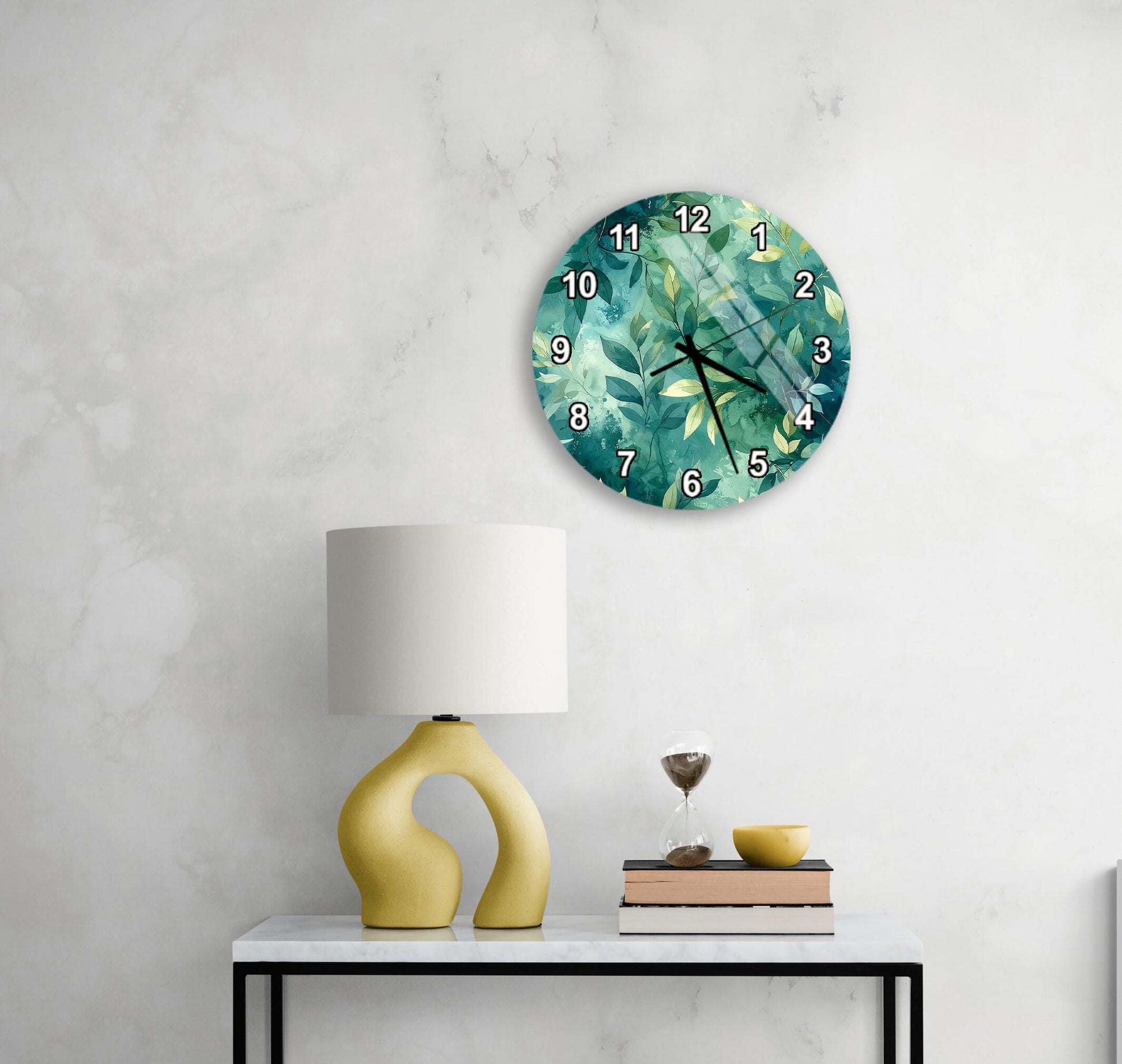 a white wall with a round clock displaying a tropical plant design, a yellow lamp on a white table, and a stack of books and a glass of wine on the table.