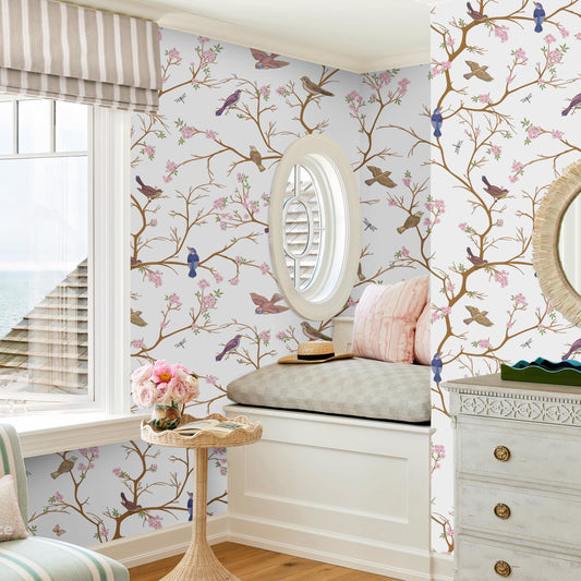 a cozy and charming bedroom with a large window overlooking the ocean, a floral wallpaper, and a round window seat. The room is decorated with a mix of pink and white floral patterns, and the overall color scheme is predominantly white and beige.