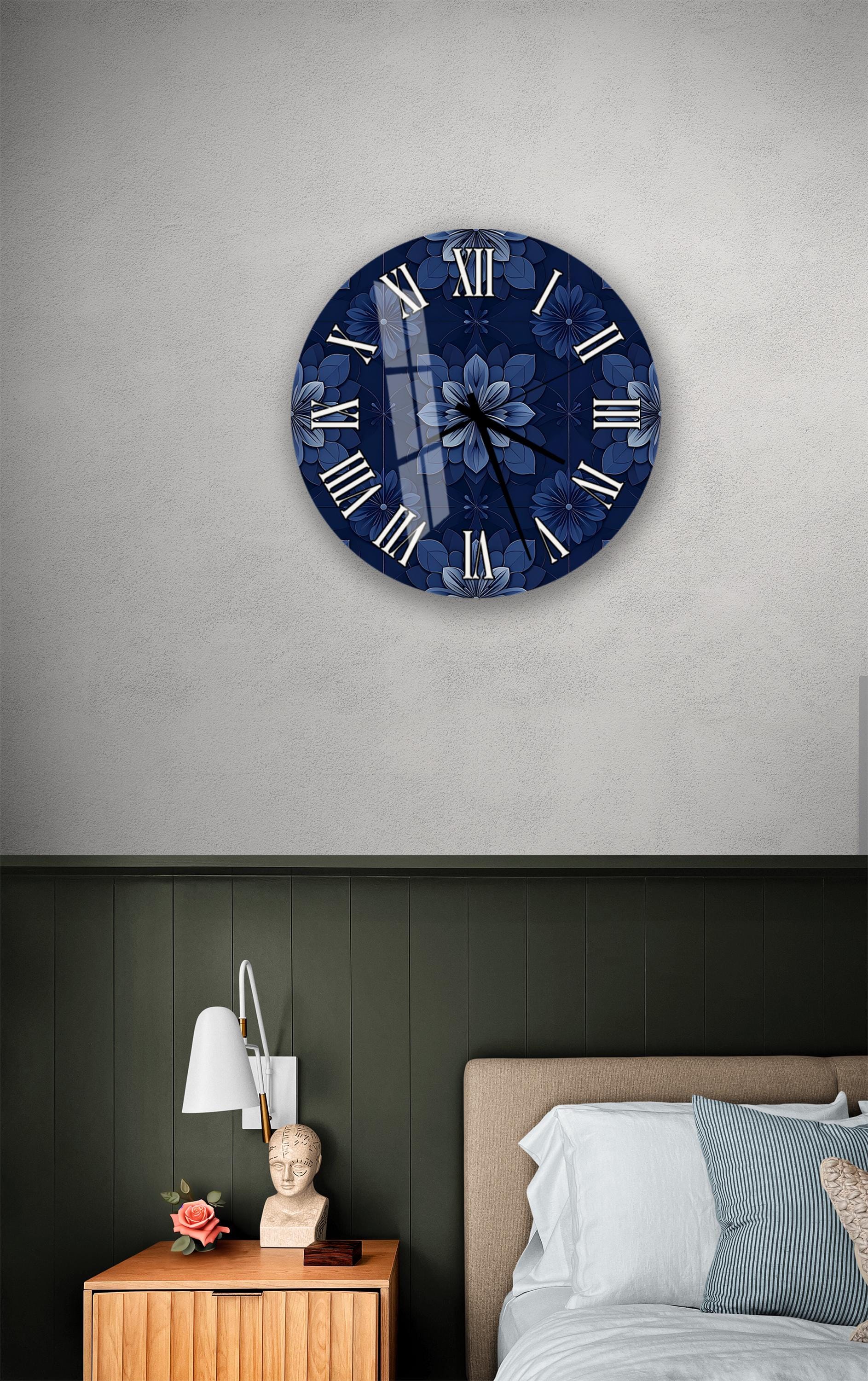 a bedroom setting with a blue floral wall clock hanging above a bed. The clock has a white face with black Roman numerals and a blue floral design. The room has a green wall, a wooden nightstand with a lamp, and a bed with white sheets and pillows.