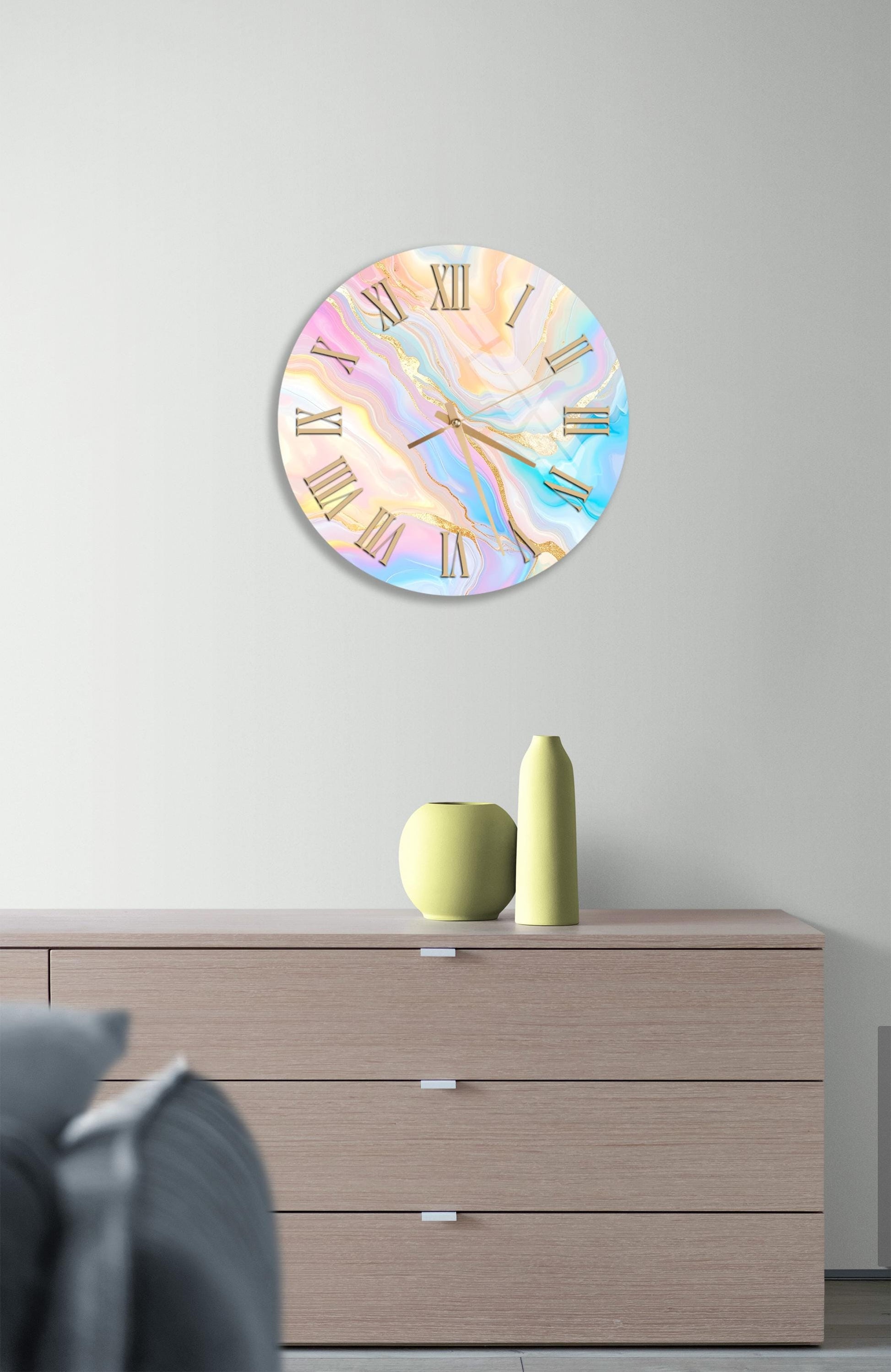 a wall clock with a marble-like design, mounted on a wall above a wooden dresser. The dresser has three drawers and contains a yellow vase and a small green pot.