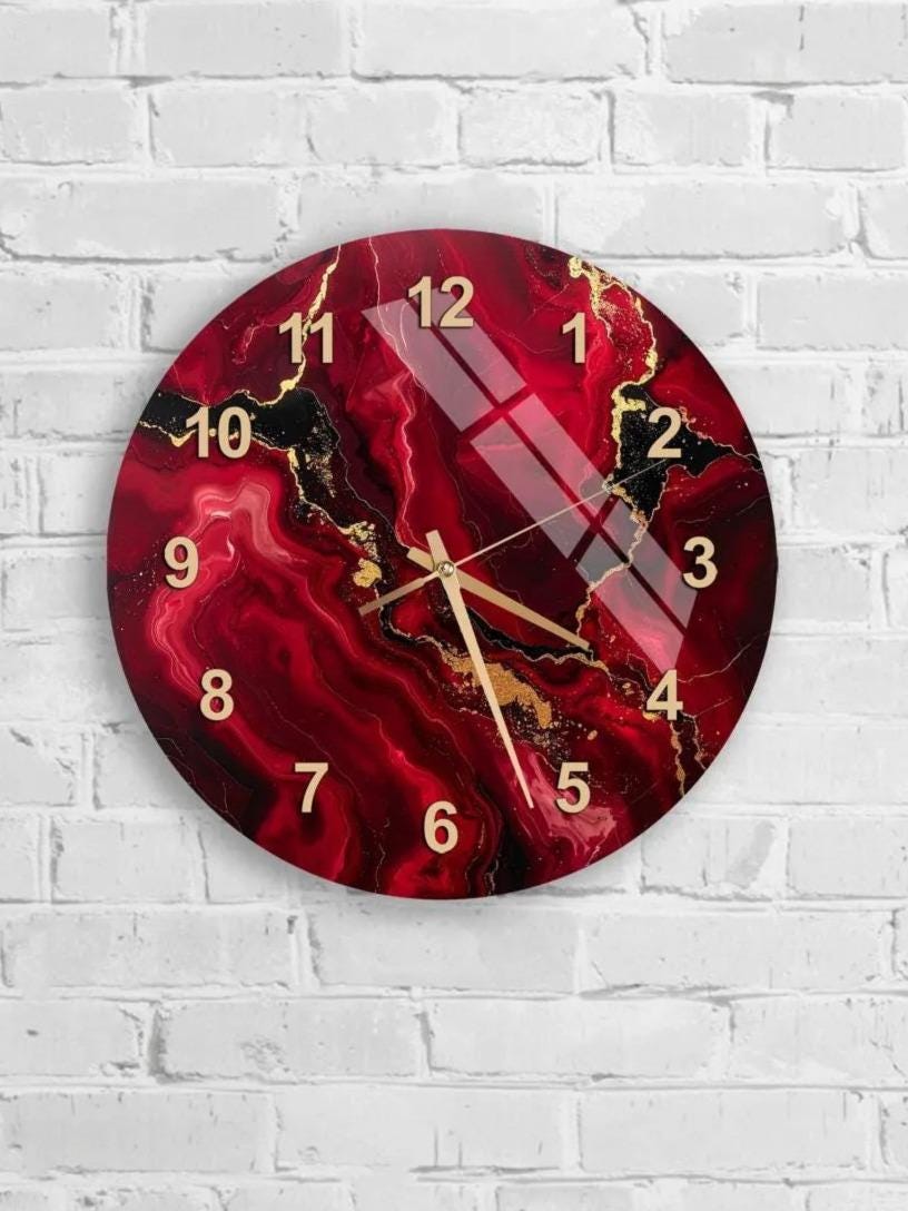 A wall clock with a marbled red and gold design, mounted on a white brick wall.