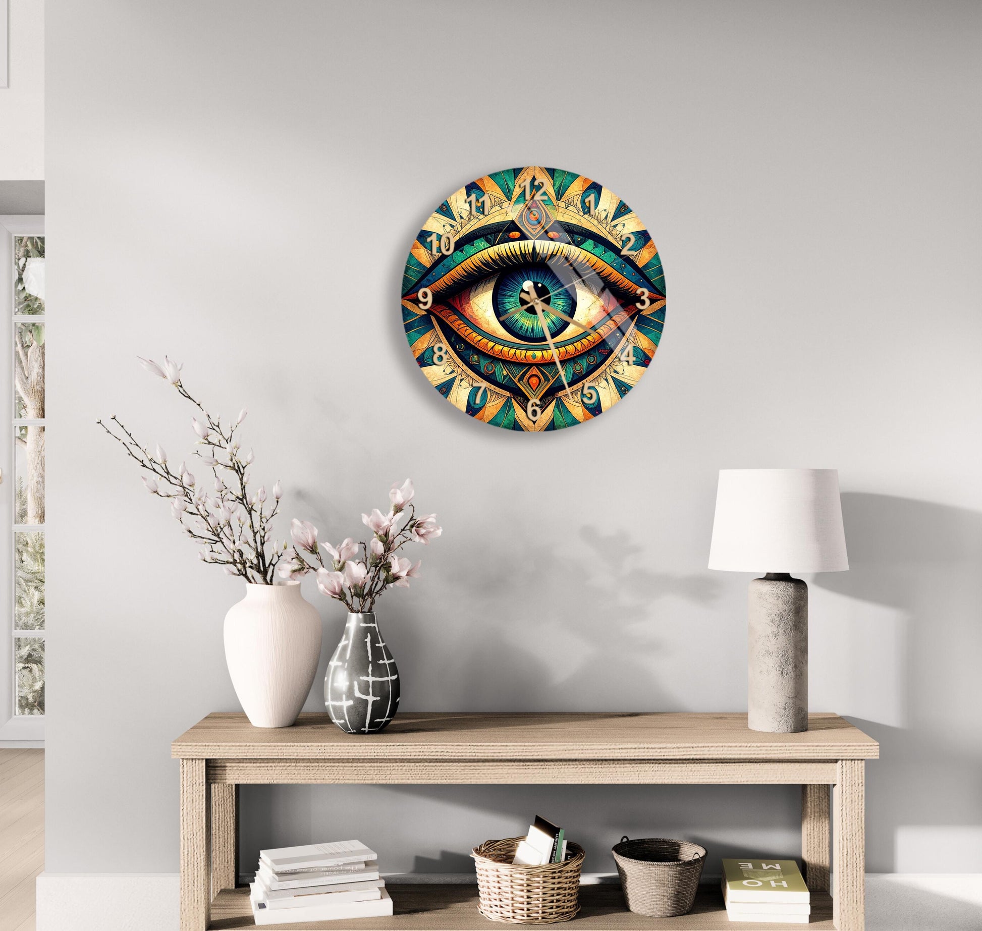 a wall clock with an eye design, a wooden table with a lamp, a vase with flowers, and some books on a shelf.