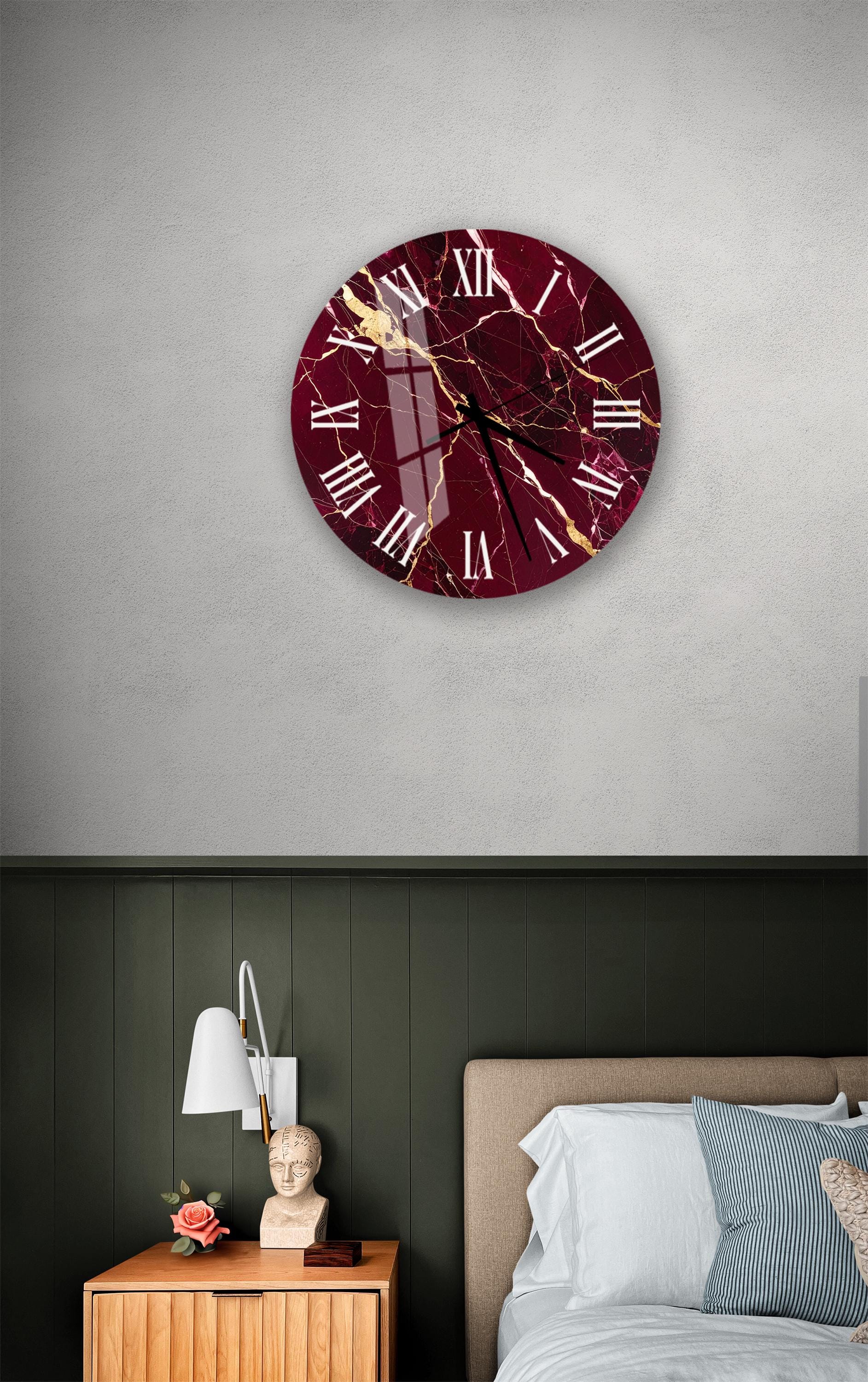 a bedroom setting with a large burgundy-colored clock hanging on the wall above a bed. The clock has a white face and gold accents, adding a touch of elegance to the room. The bed is neatly made, and there is a nightstand with a lamp and a vase of flowers nearby. The overall scene conveys a sense of comfort and relaxation.