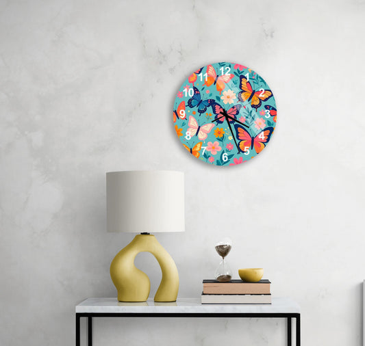 a white table with a yellow lamp, a white vase, and a stack of books. Above the table, there is a round clock with a colorful butterfly design on it.