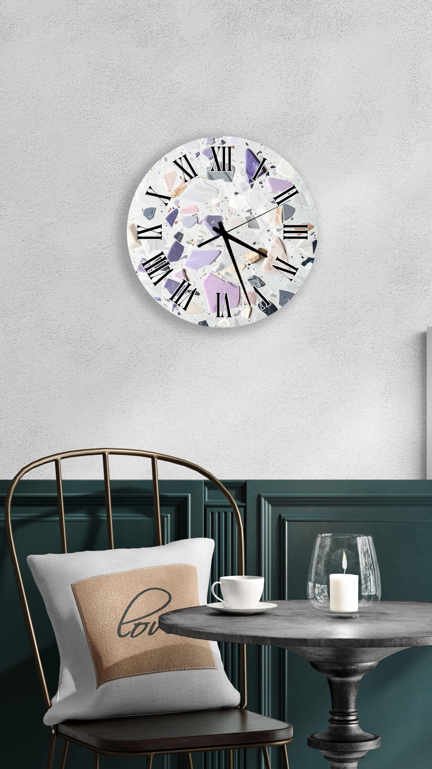 a modern and stylish interior design with a round wall clock displaying a colorful mosaic pattern, a white table with a candle and a cup, and a black metal chair with a pillow.
