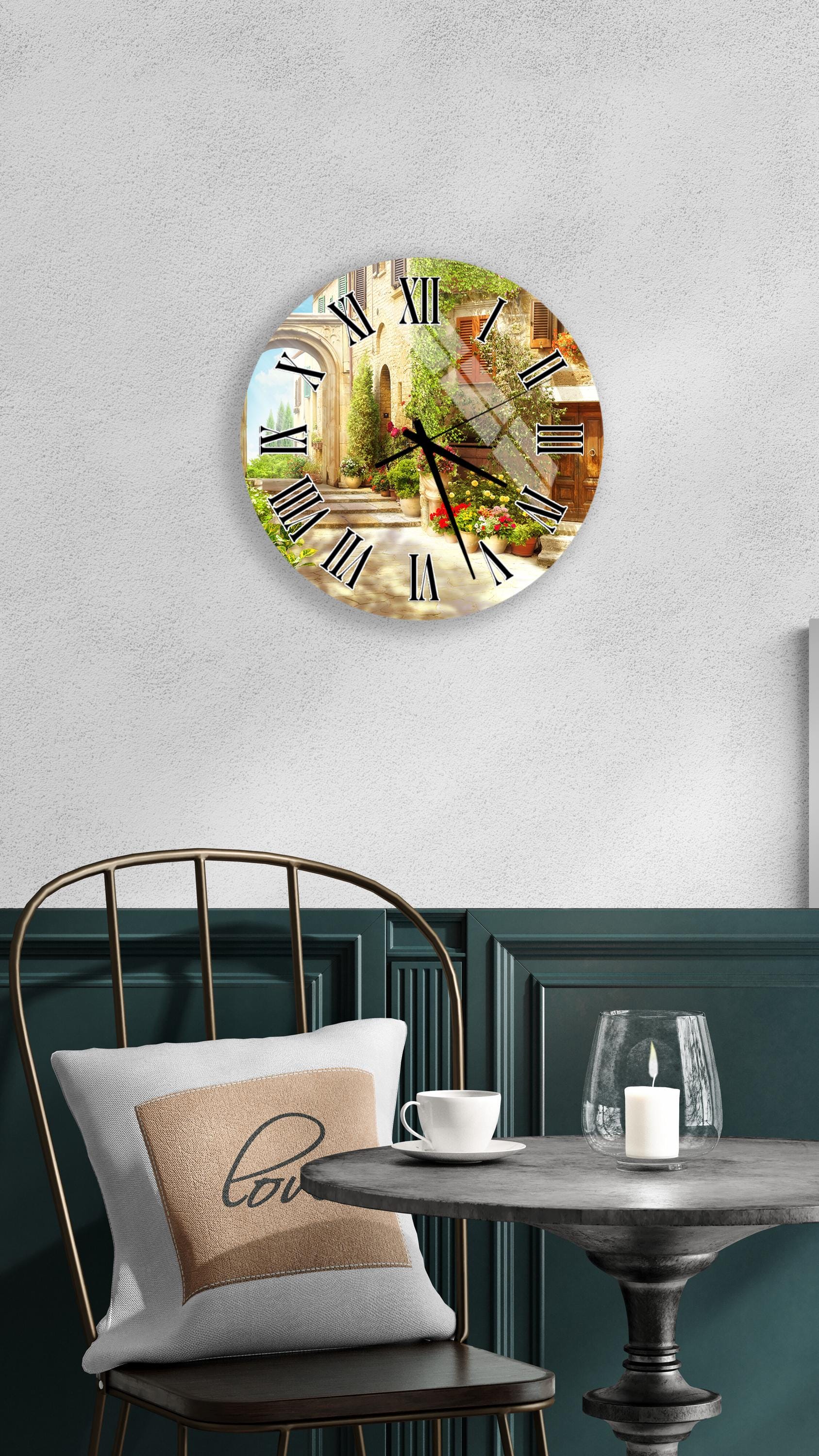 a wall clock with a scenic image of a town or village, mounted on a wall above a table with a white tablecloth and a candle.