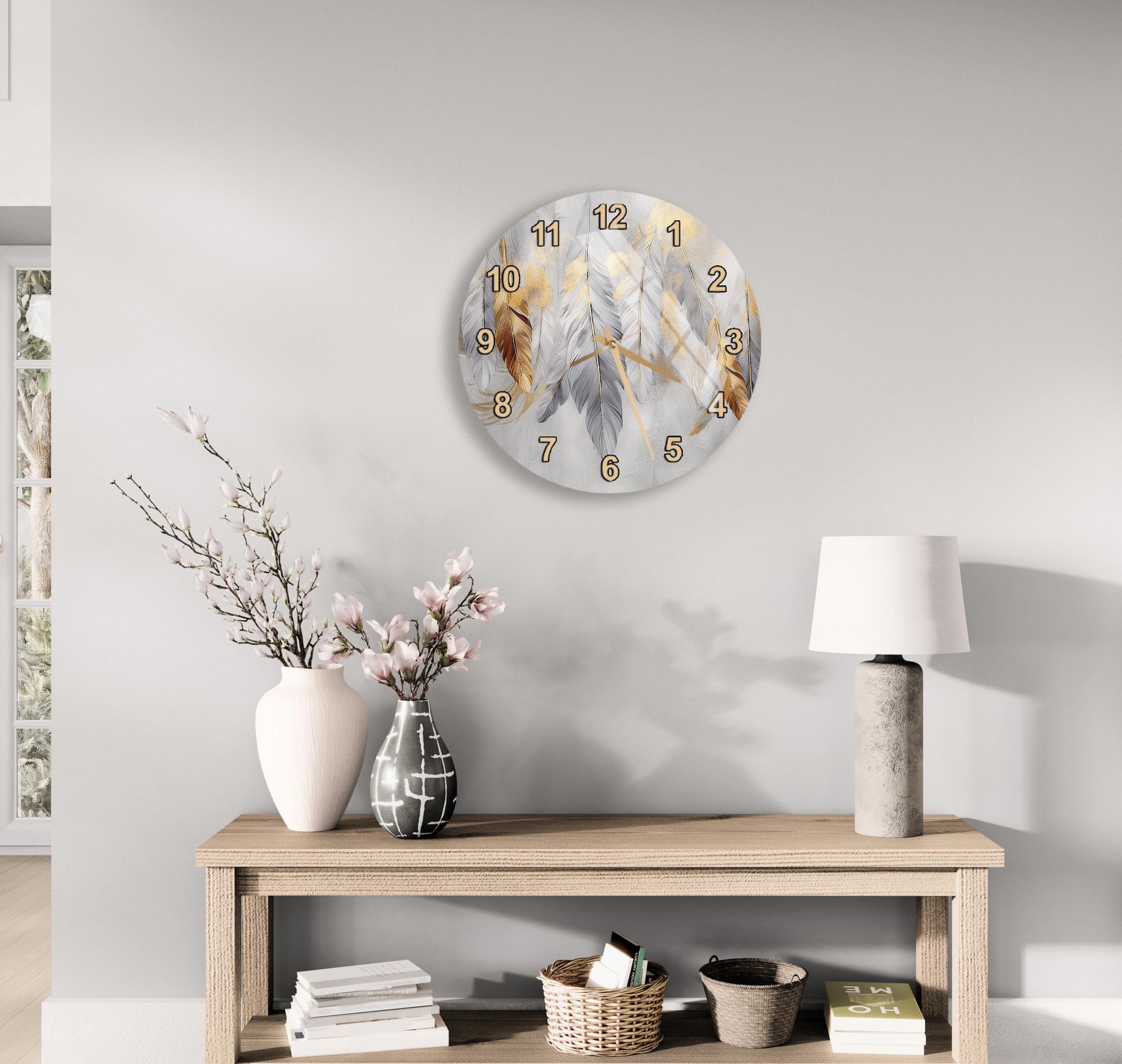 a modern living room with a wooden console table, a round wall clock with a feather design, a lamp, a vase with pink flowers, and a stack of books.