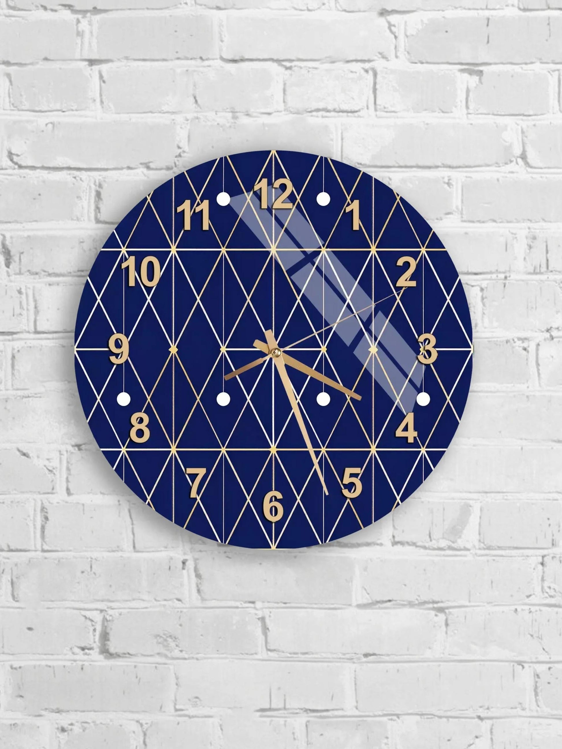 A blue and gold geometric clock with a diamond pattern and gold numbers is mounted on a white brick wall.