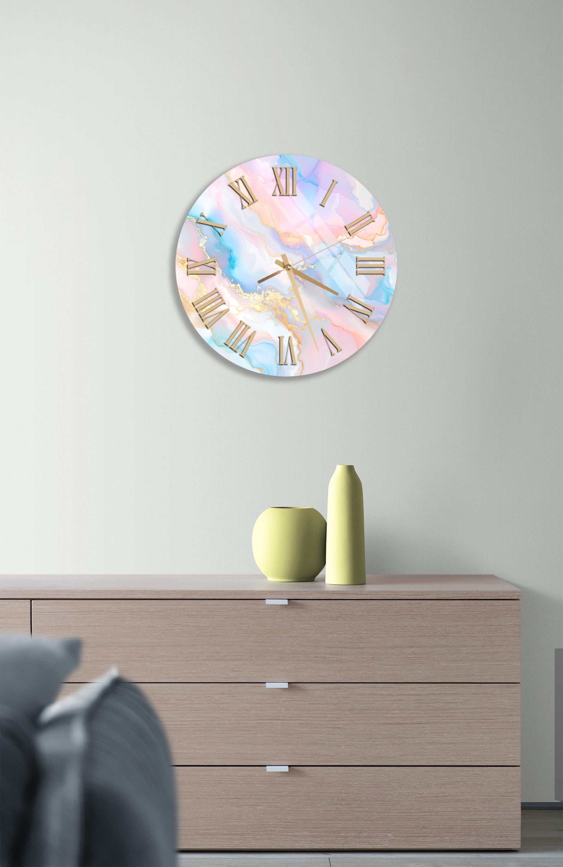 a wall clock with a marble-like design, mounted on a wall above a wooden dresser. The dresser has three drawers and contains a yellow vase and a small green pot.