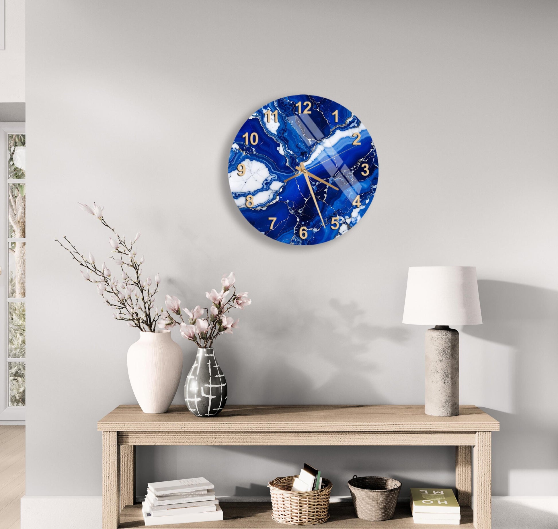 a modern living room with a wooden table, a white vase with pink flowers, a round wall clock with a blue and white marble design, and a lamp on the table.