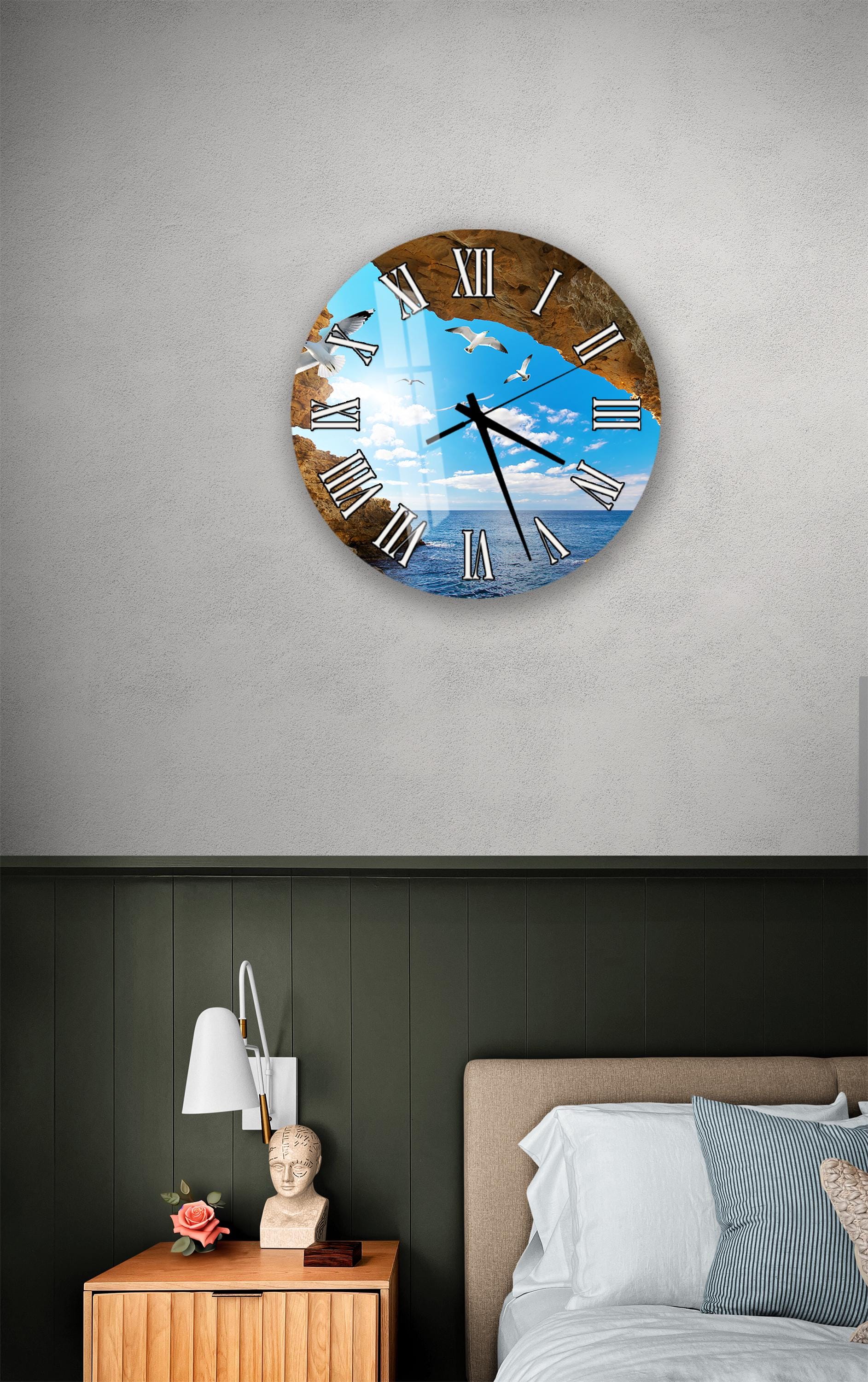 a wall clock with a beach scene on its face, mounted on a wall above a bedside table with a lamp and a small statue.