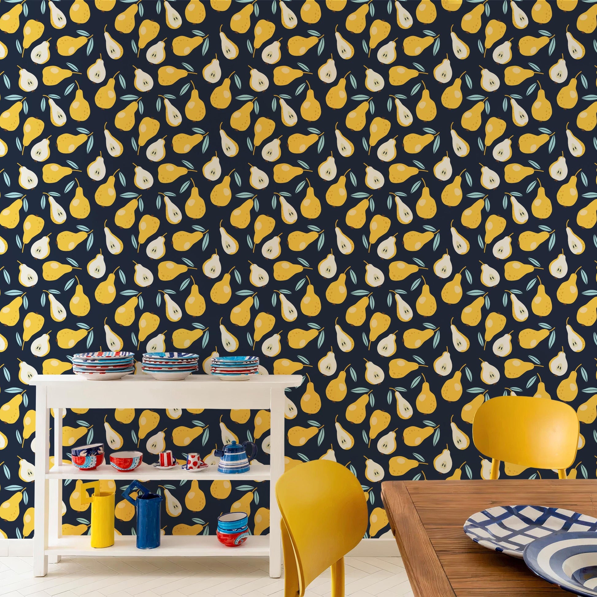 a kitchen with a white table and yellow chairs, set against a wall with a repeating pattern of yellow pears. The table has various dishes and utensils on it, and the chairs are positioned around the table.