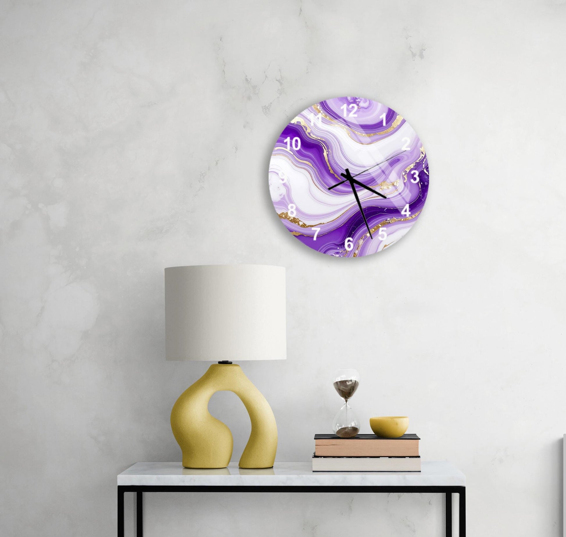 a white wall with a round clock displaying a purple marble design, a yellow lamp, a stack of books, and a glass of wine on a white table.