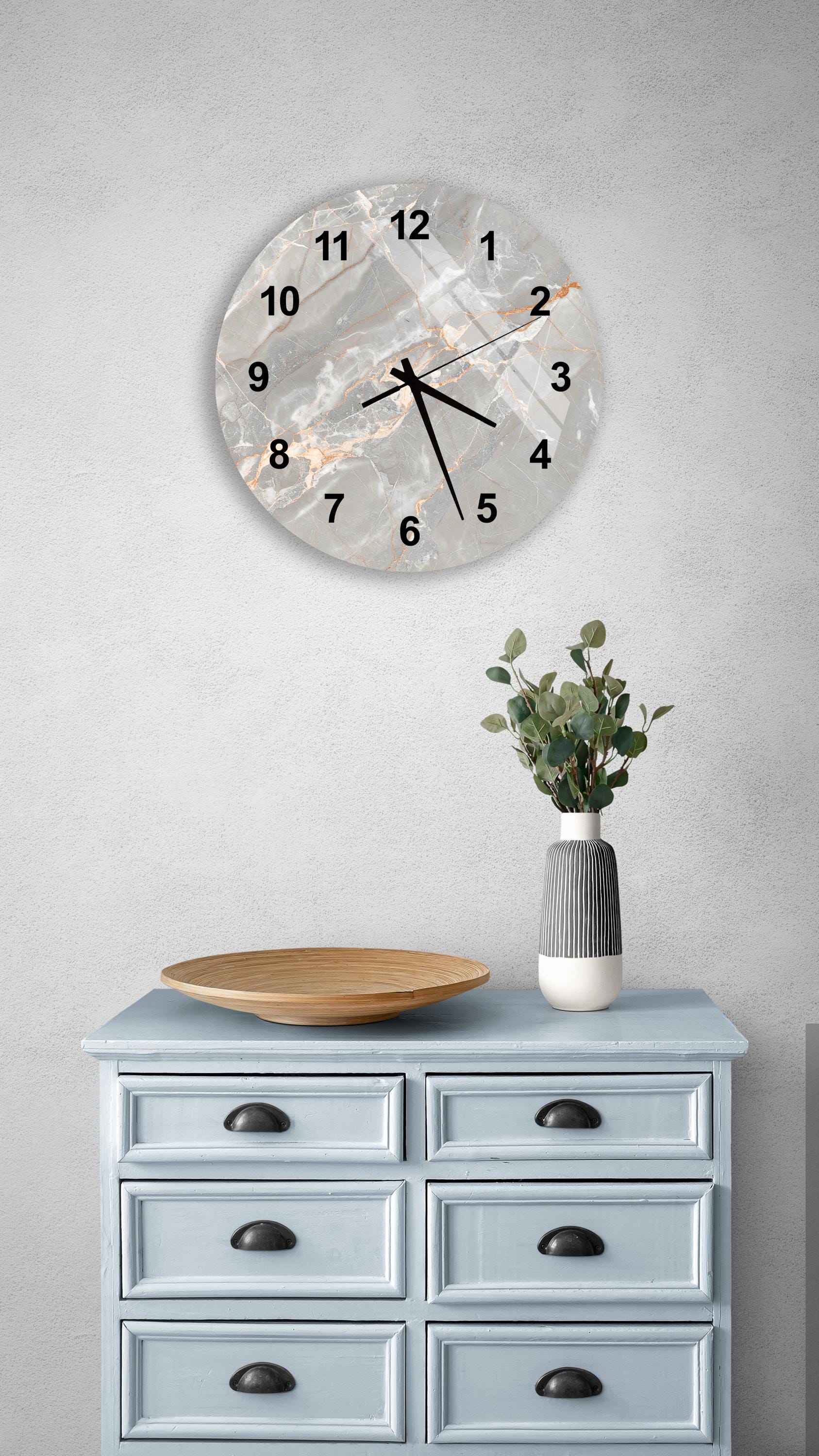 a wall clock with a marble-like design, a wooden bowl, and a vase with greenery on a light blue dresser.