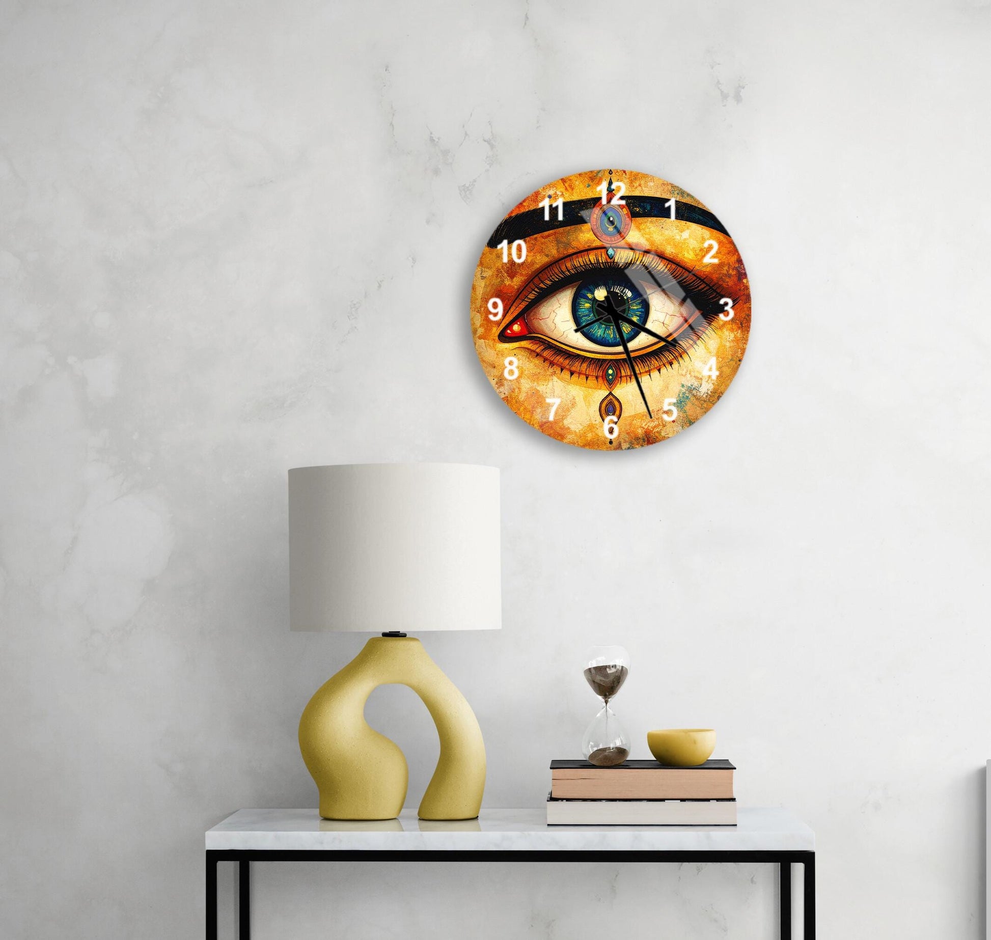 a wall clock with an eye design, a yellow table lamp, a stack of books, and a glass of water on a white table.