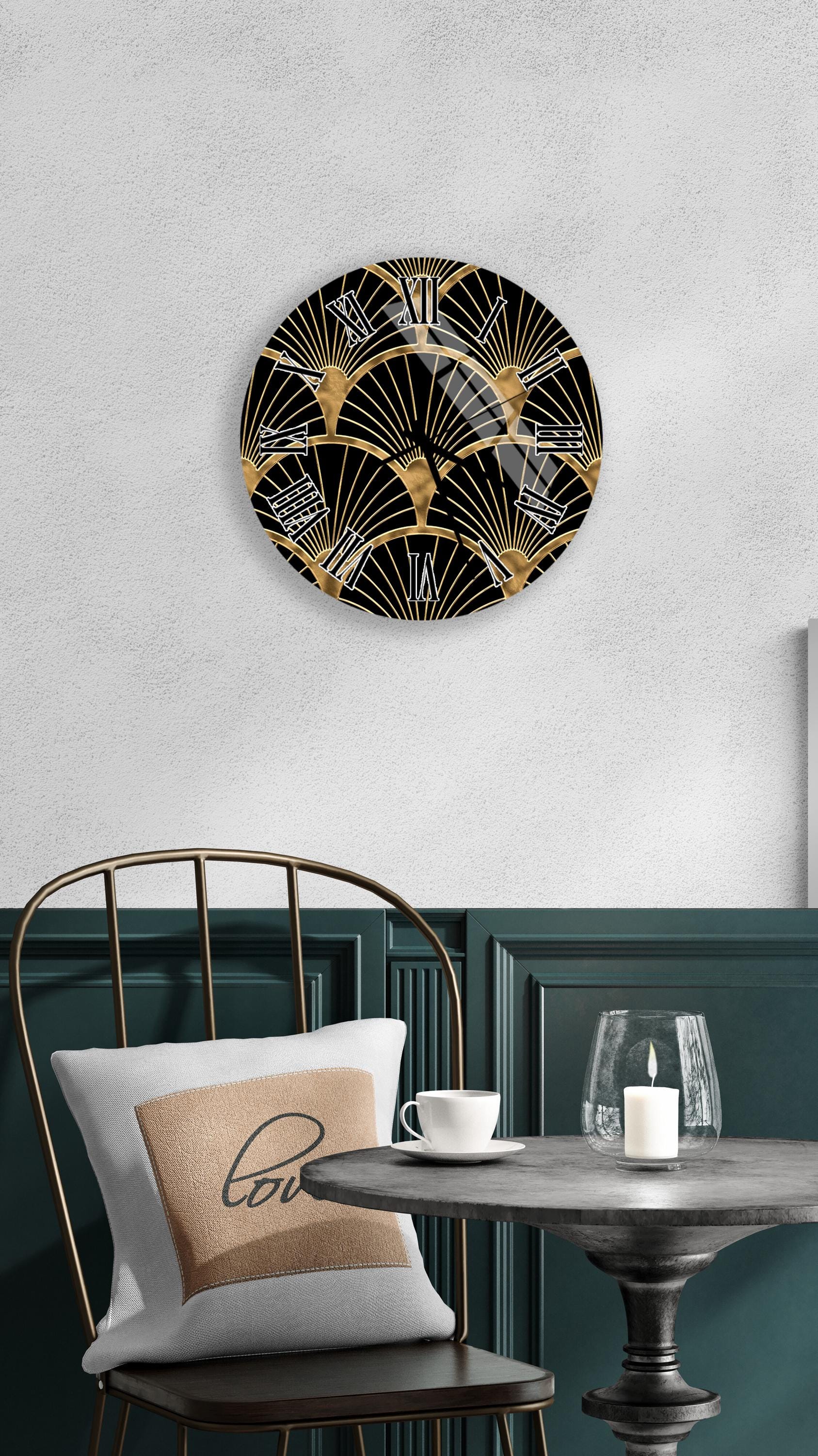 a modern black and gold wall clock with a repeating fan-like pattern, mounted on a white wall above a black chair with a white pillow. In front of the chair, there is a small table with a glass and a candle, creating a cozy and inviting atmosphere.