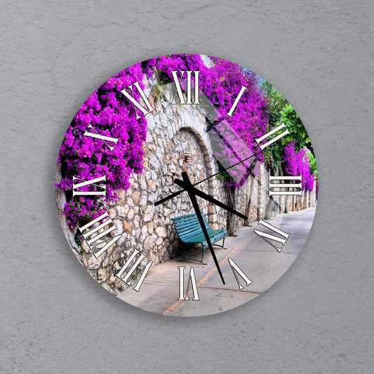 A clock with a design featuring a stone archway and a bench, surrounded by purple flowers.