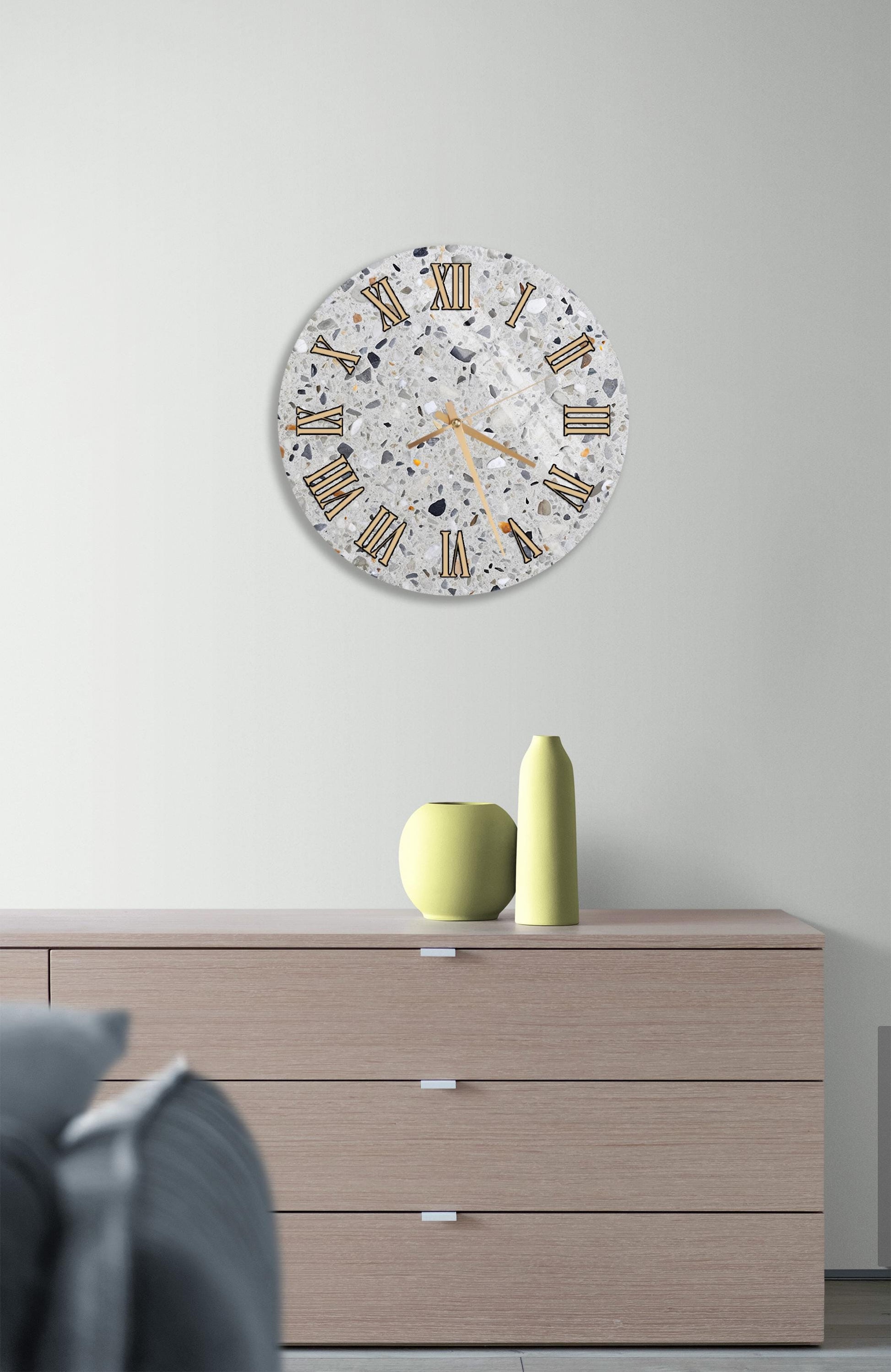 a modern interior design with a large round wall clock displaying Roman numerals, a wooden dresser with a yellow vase and a small green pot, and a gray couch in the background.