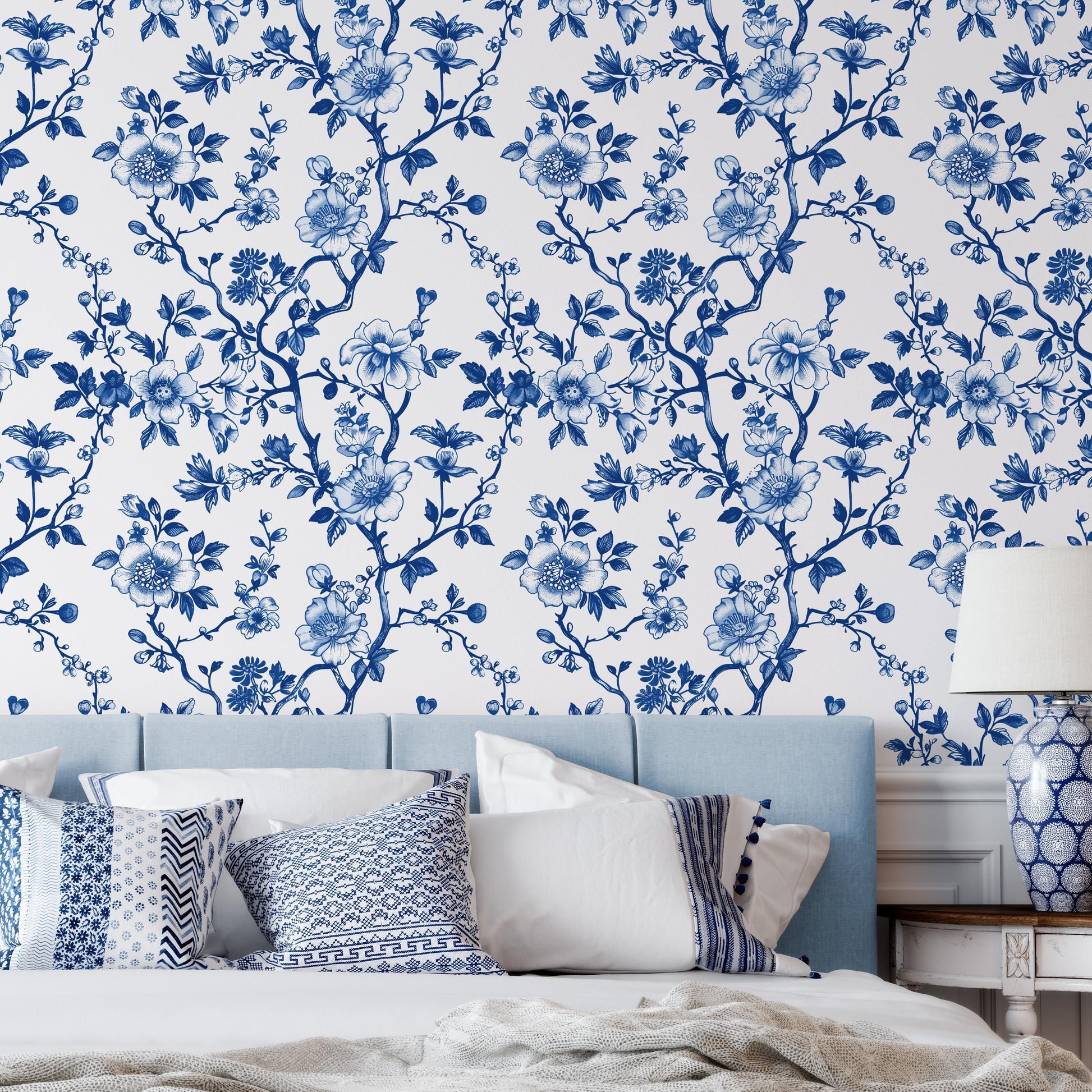 a bedroom with a blue and white floral wallpaper on the wall behind a bed with white pillows and a blue headboard.